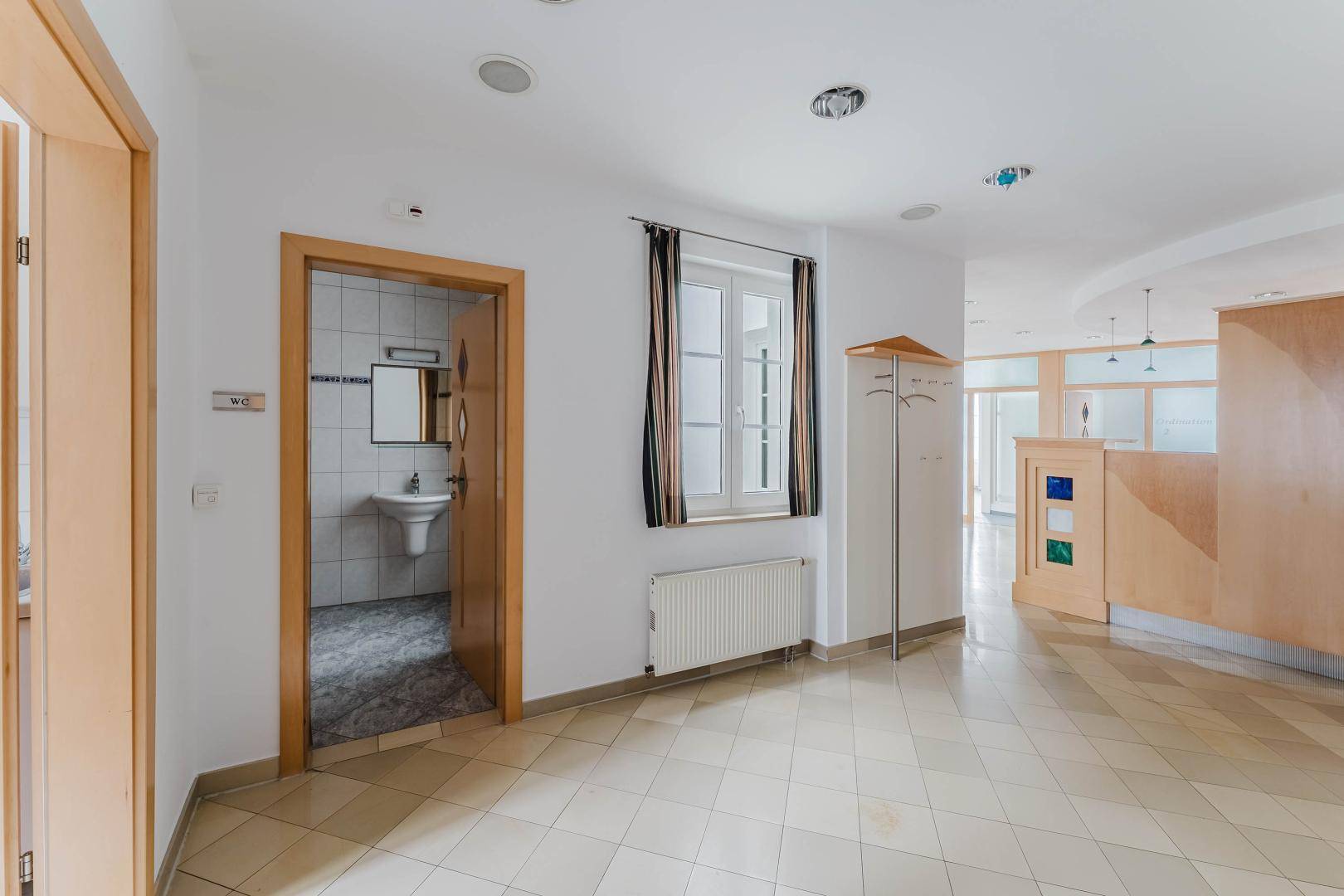 Heller Empfangsbereich mit Fliesenboden, Garderobe und Zugang zu einer Toilette.