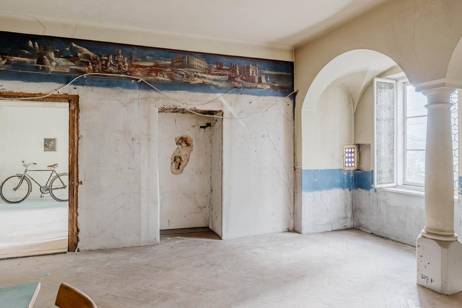 Historischer Raum mit Bögen, Säulen und einem Wandgemälde, Blick in einen Nebenraum.