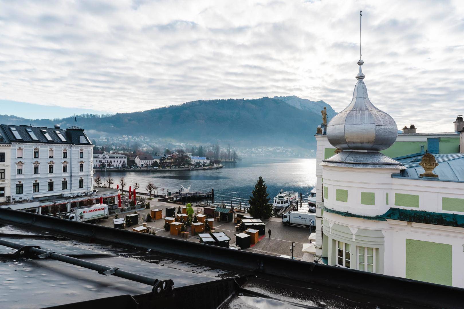 Panoramablick über den See und die Stadt von einem Dach aus, mit Bergen im Hintergrund.