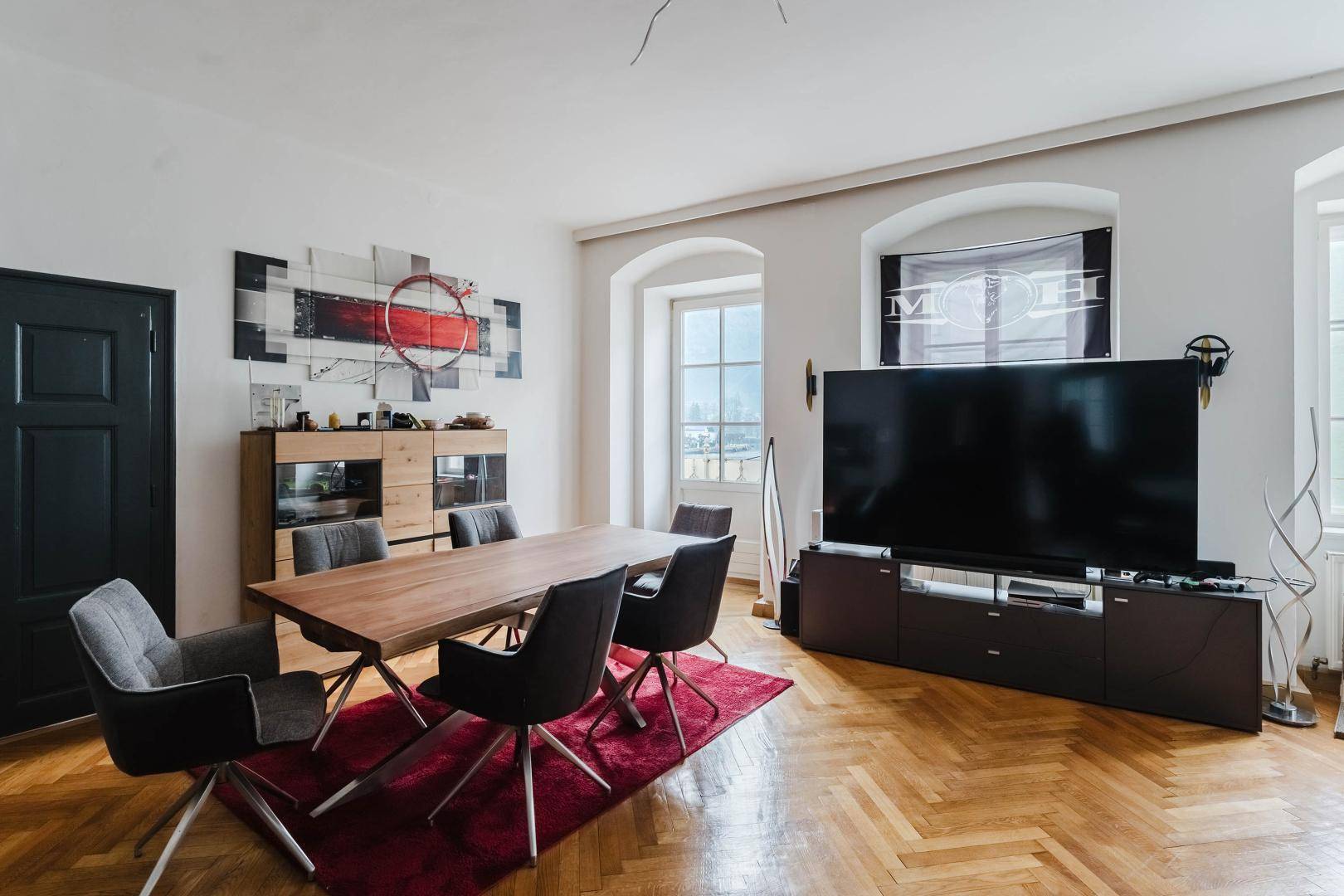 Geräumiger Wohn- und Essbereich mit Holztisch, Parkettboden und großer Fensterfront.