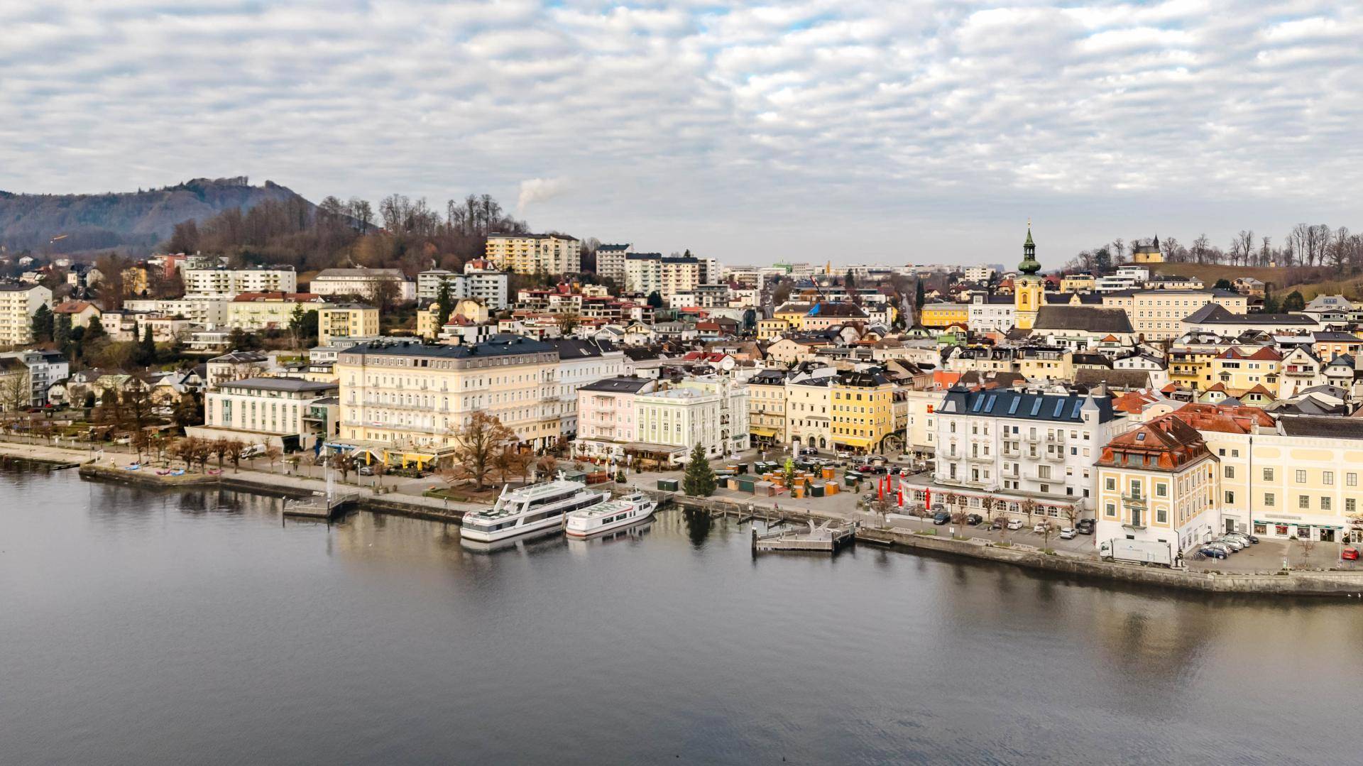 Panoramablick auf die Stadt am See mit historischen Gebäuden und Bergen im Hintergrund.