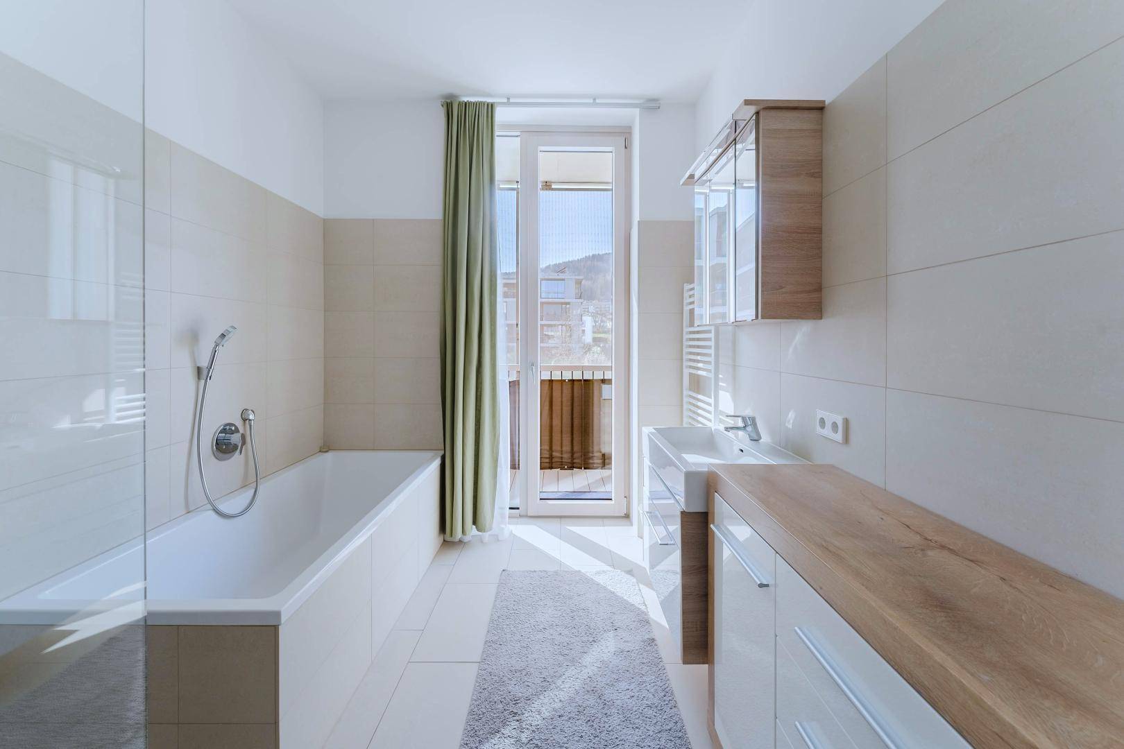 Modernes Badezimmer mit Badewanne, Waschtisch und Zugang zu einem kleinen Balkon.