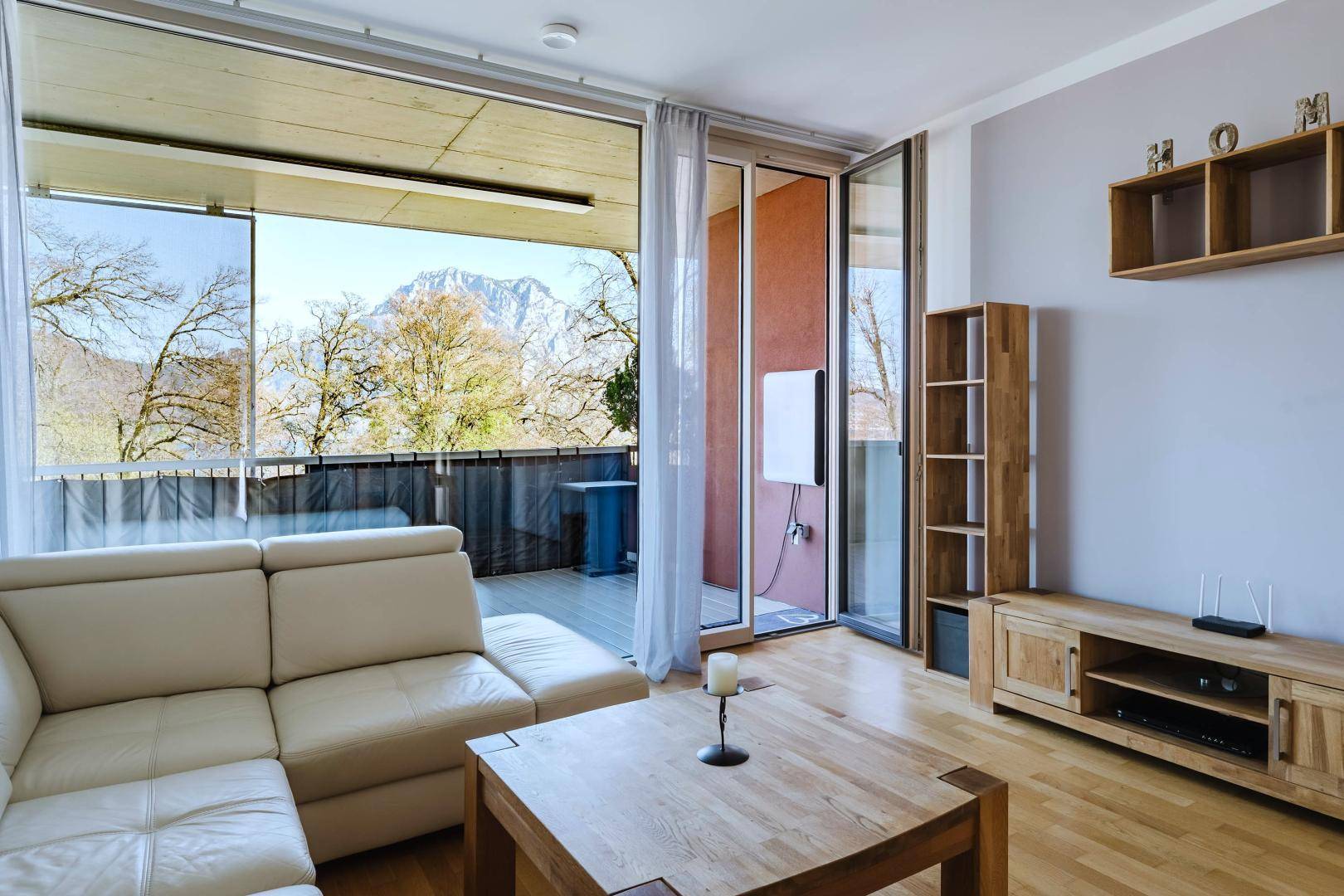 Helles Wohnzimmer mit beiger Ledercouch, Holztisch und Zugang zu einem Balkon mit Bergblick.