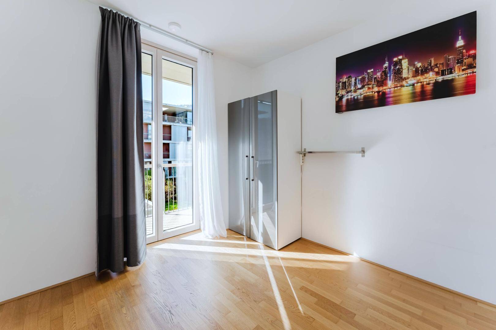 Geräumiges Schlafzimmer mit Holzboden, weiß gestrichenen Wänden und Zugang zum Balkon.