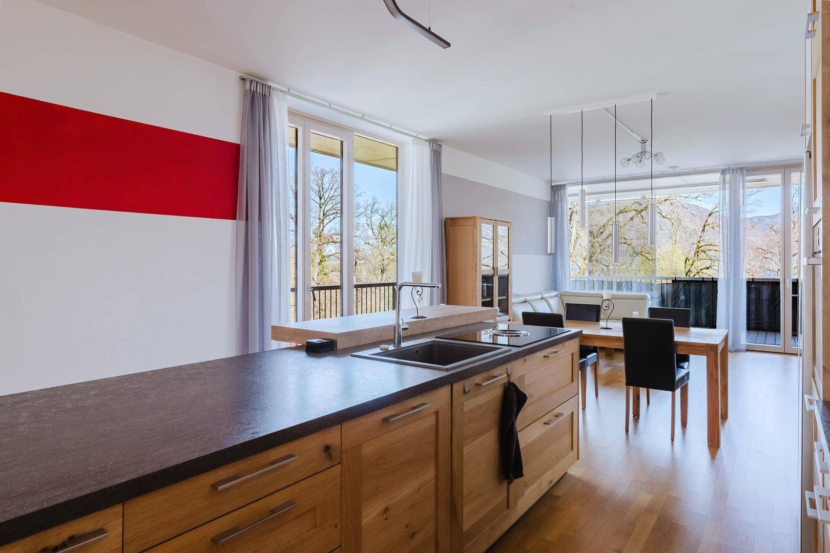Funktionale Küche mit Holzfronten, dunkler Arbeitsplatte und Blick in den Wohnbereich.