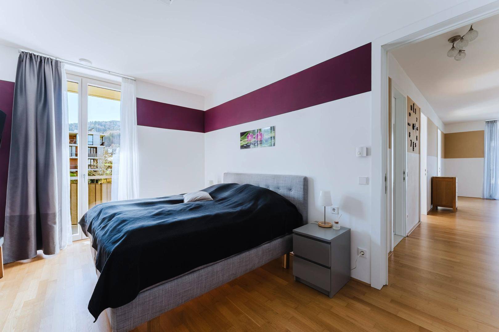 Modernes Schlafzimmer mit Doppelbett, Holzboden und Zugang zu einem Balkon.