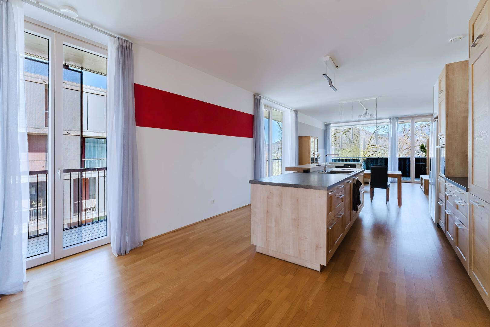 Offener Wohnbereich mit Holzboden, Kücheninsel und Zugang zu einem Balkon.