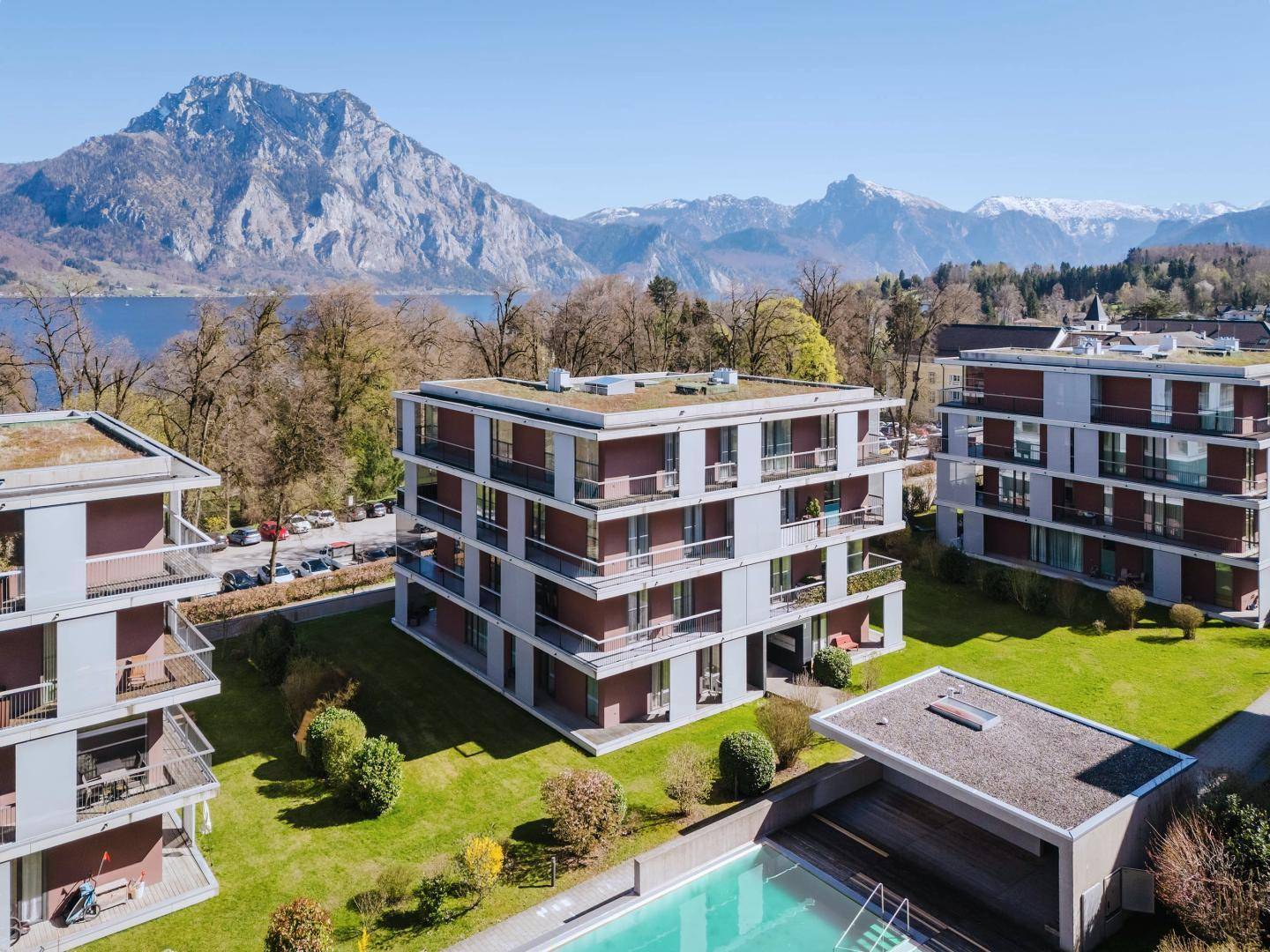 Wohnanlage mit modernen Gebäuden, einem Gemeinschaftspool und beeindruckendem See- und Bergblick.