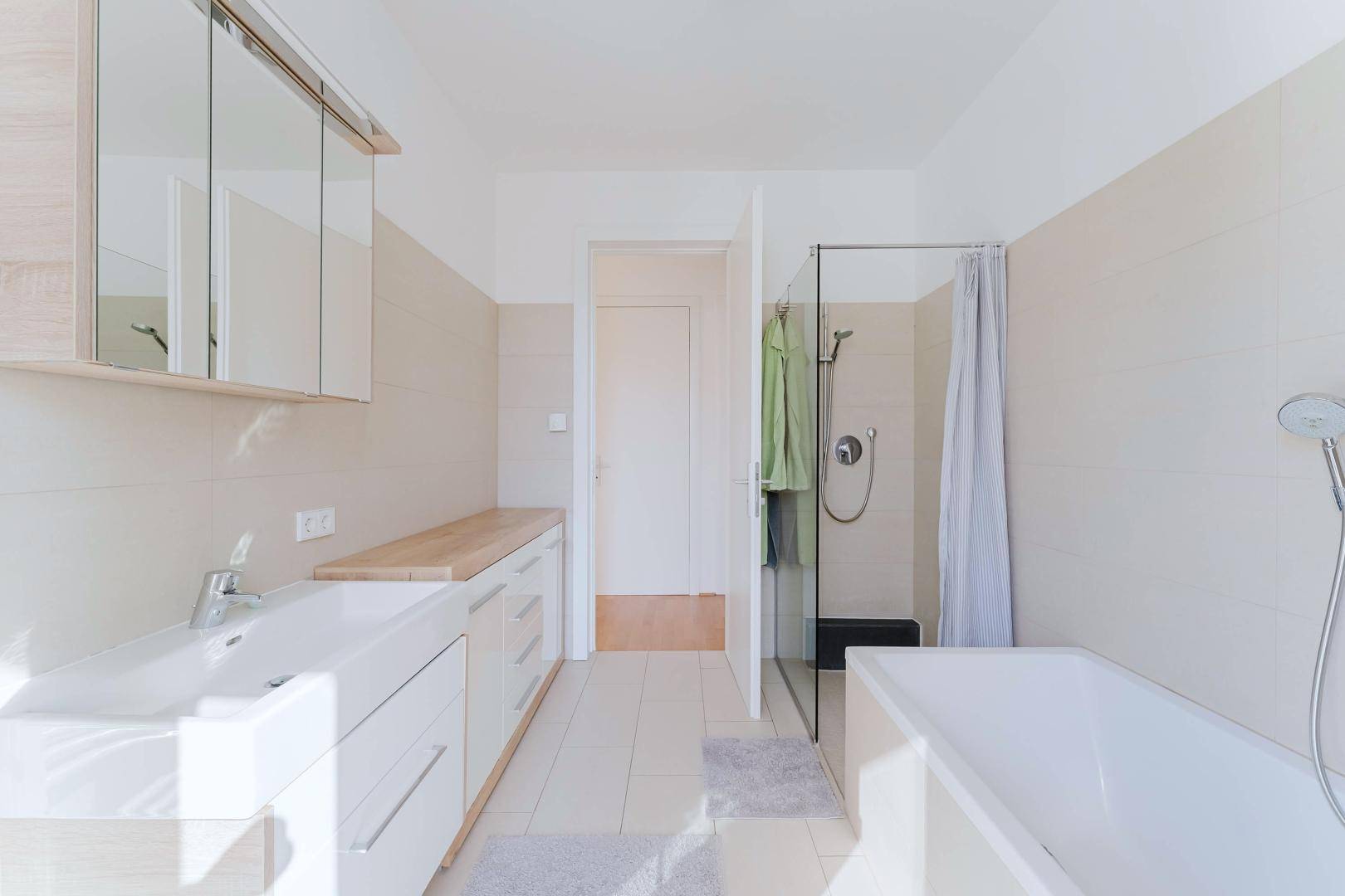 Helles Badezimmer mit Badewanne, Dusche, Waschtisch und Spiegelschrank.