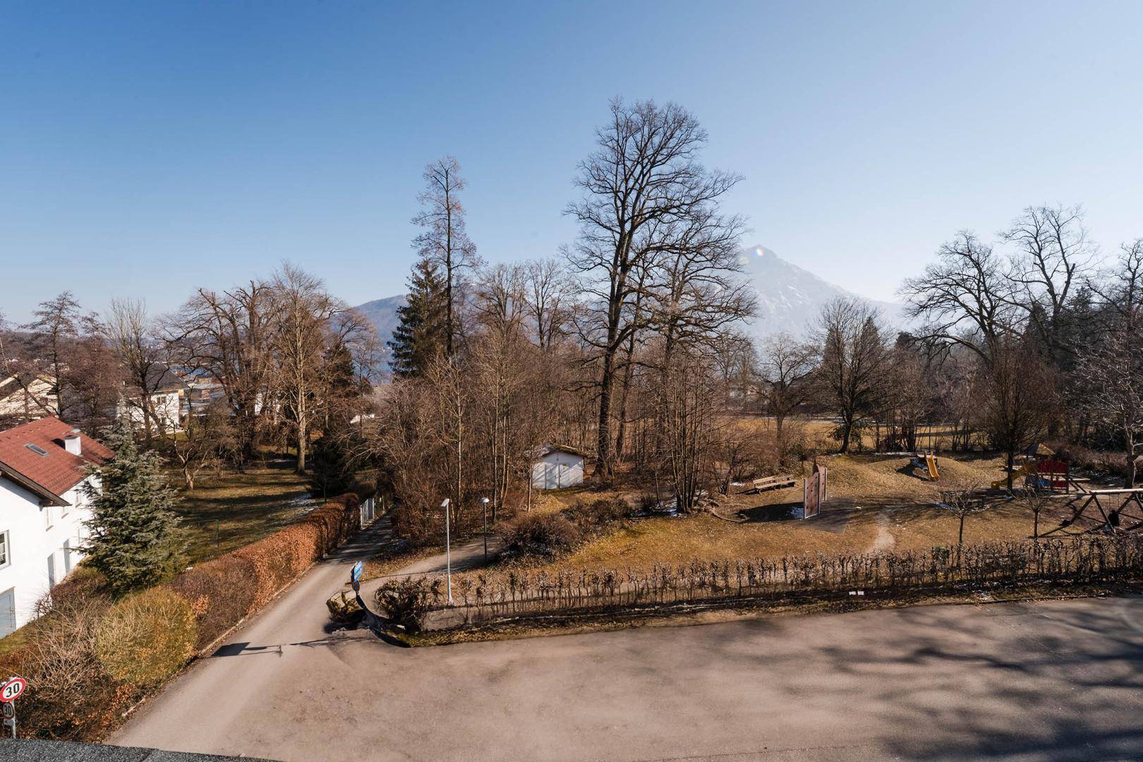 Winterlicher Ausblick auf einen Spielplatz, kahle Bäume und schneebedeckte Berge.