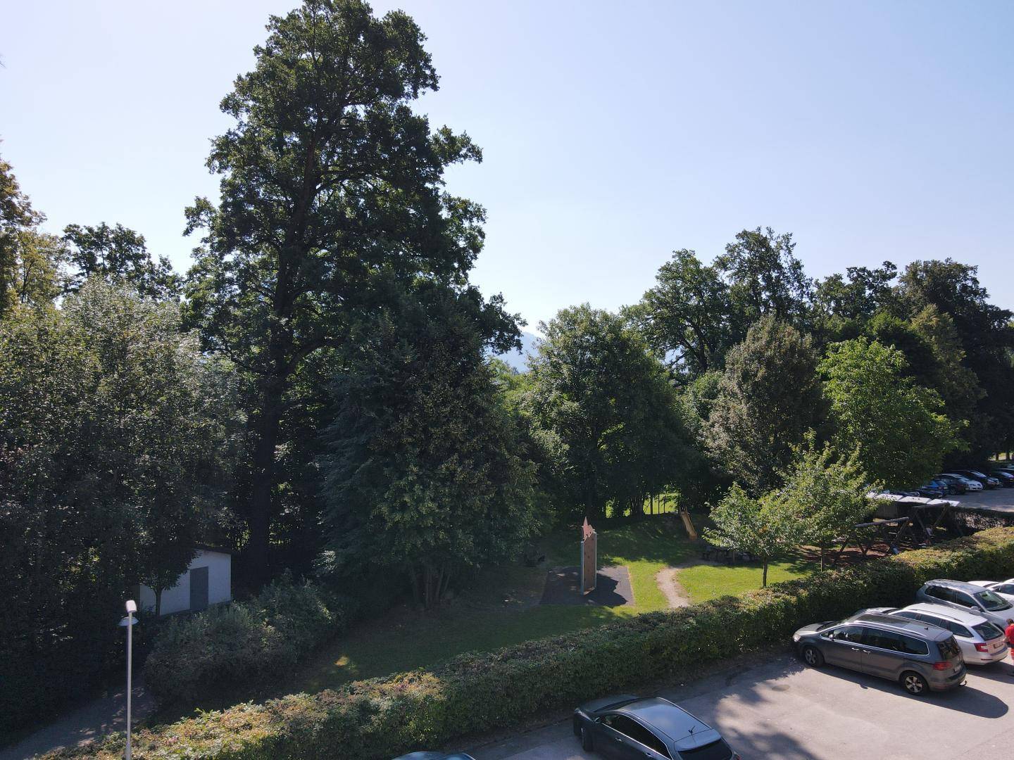 Weitläufiger Blick auf eine grüne Parkanlage mit Bäumen und einem Parkplatz.