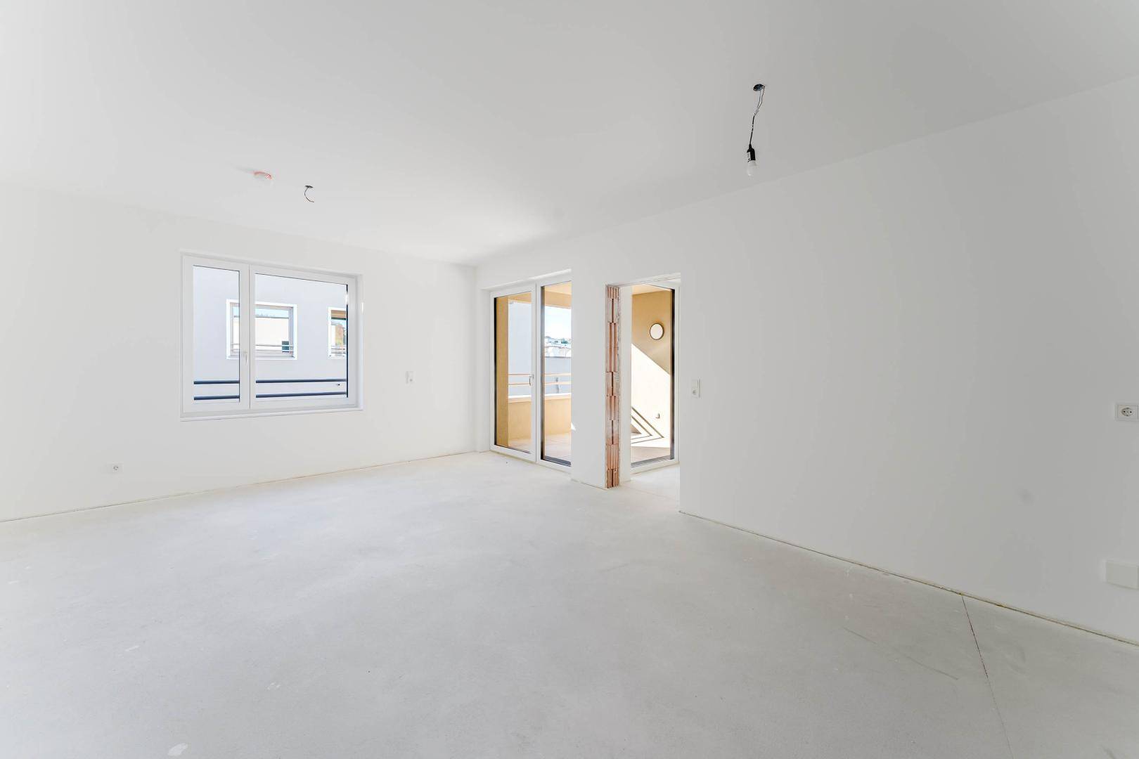 Geräumiger, unmöblierter Wohnbereich mit großen Fenstern und Zugang zum Balkon.