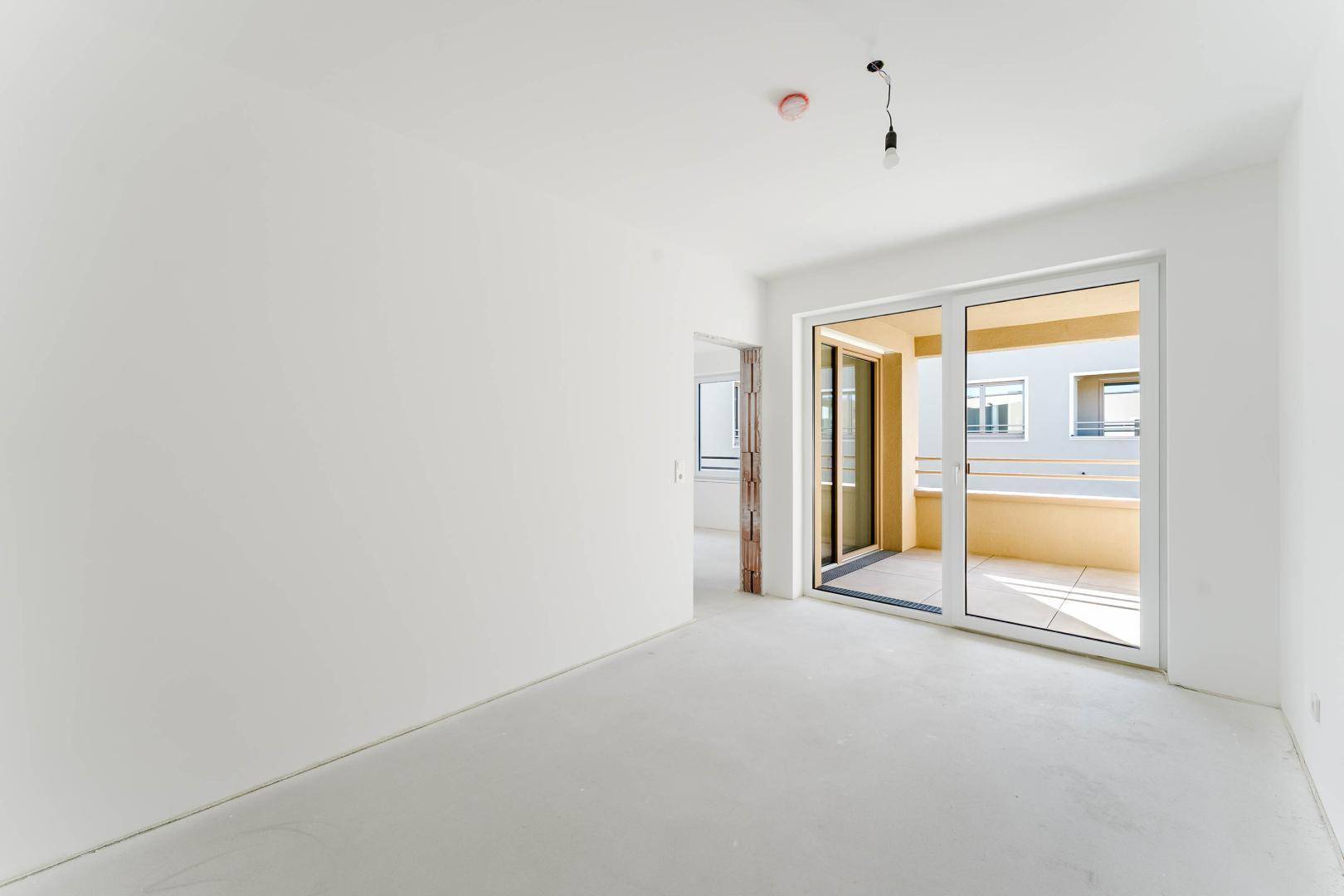 Heller, unmöblierter Raum mit Schiebetür zum Balkon und weißen Wänden.