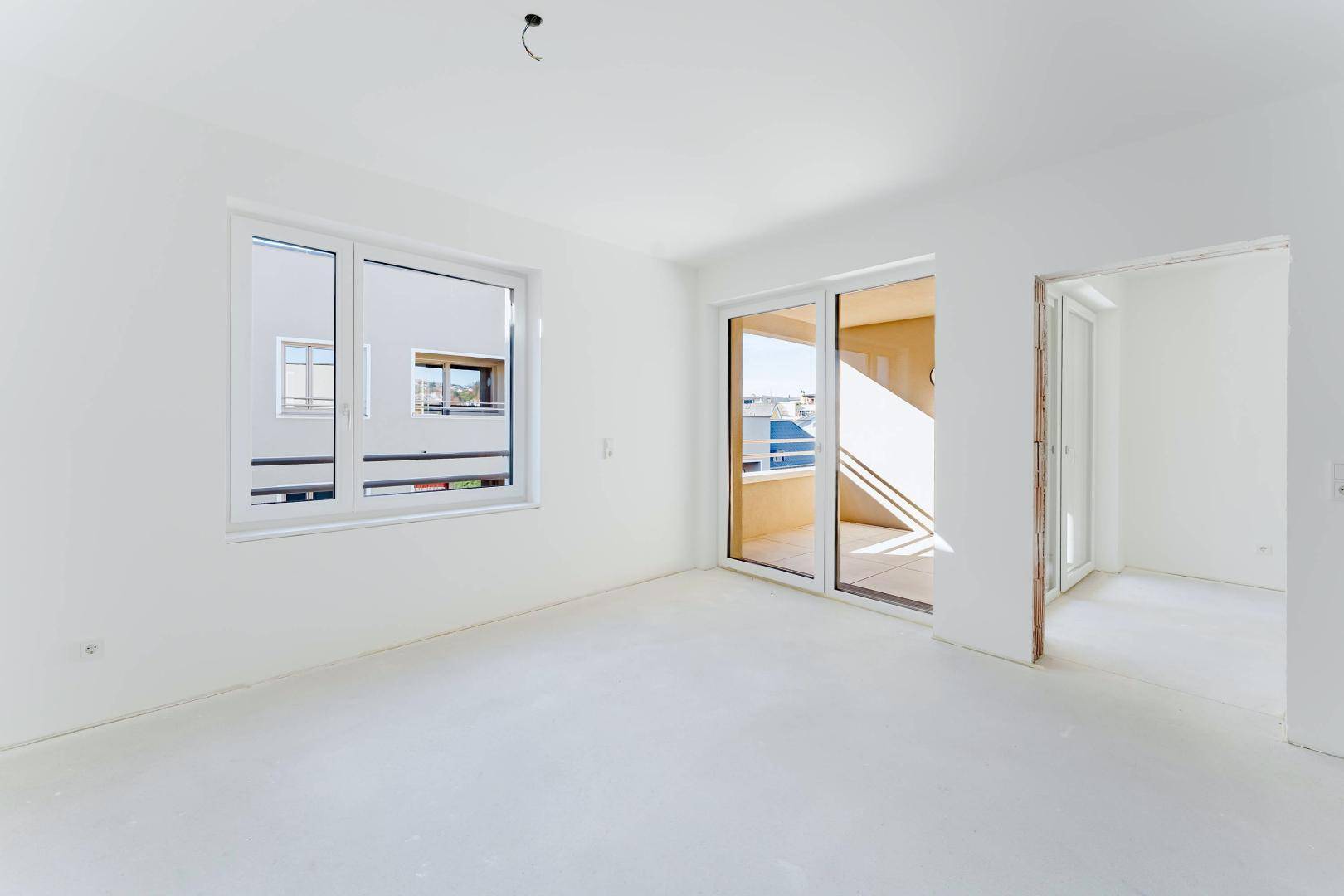 Heller, unmöblierter Wohnbereich mit Fenster und Schiebetür zum Balkon.