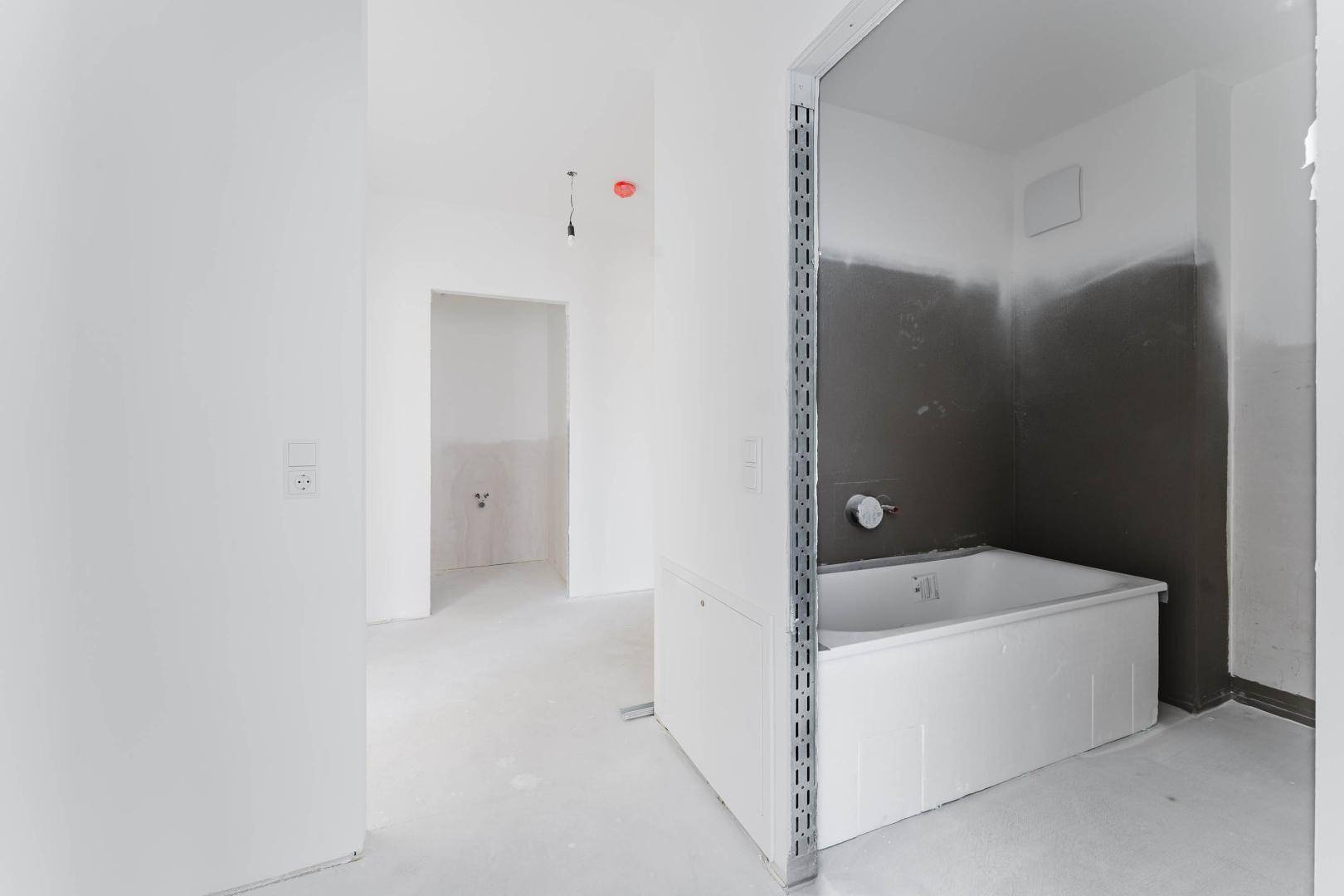 Badezimmer im Rohbau mit eingebauter Badewanne und vorbereiteten Anschlüssen.