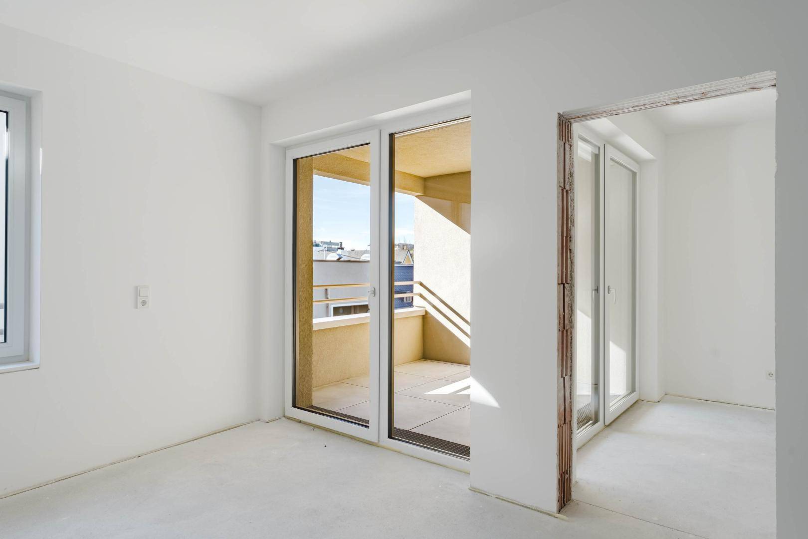 Geräumiger, unmöblierter Raum mit Schiebetüren zum Balkon und viel Tageslicht.