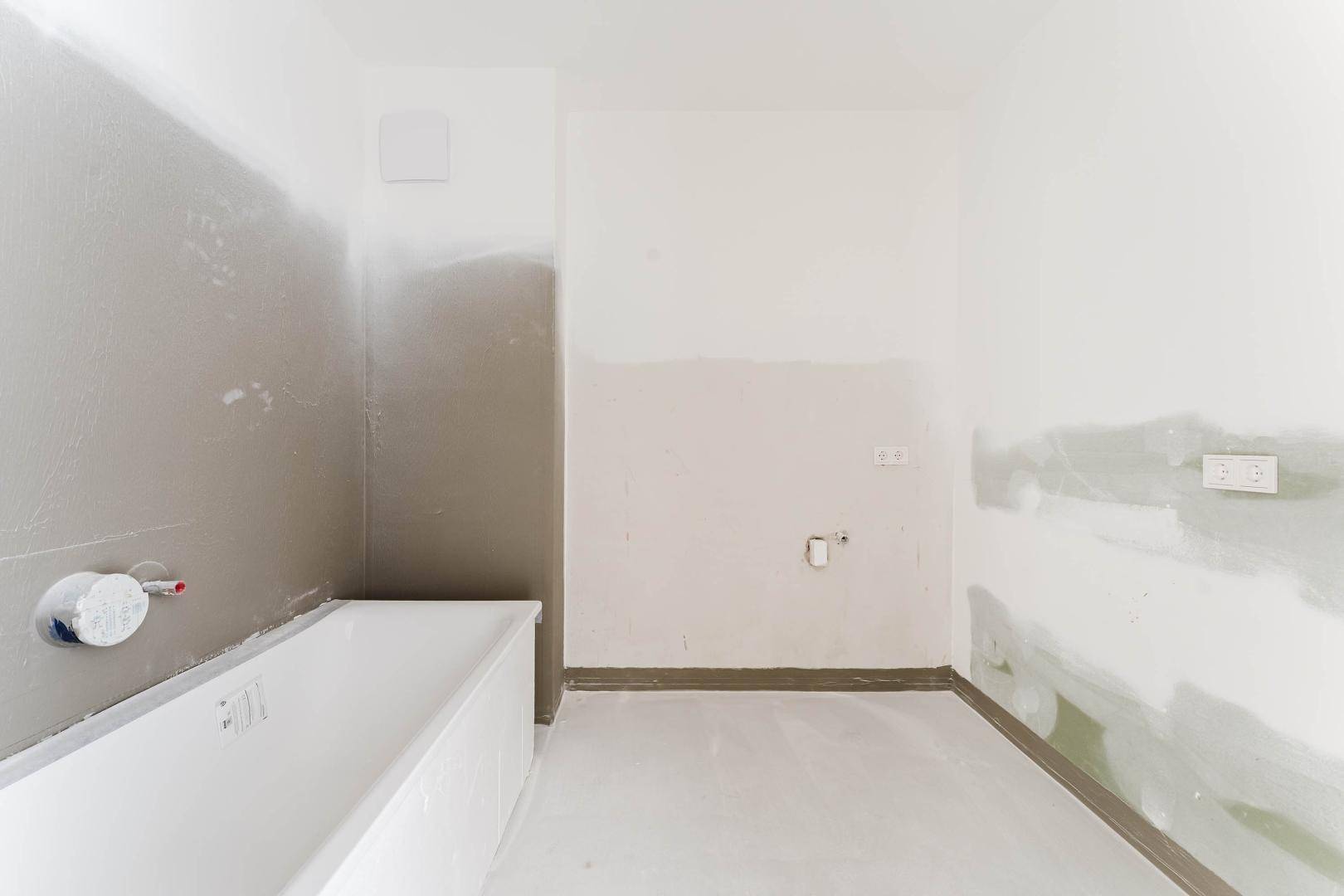 Badezimmer im Rohbau mit Badewanne und teilweise verputzten Wänden.