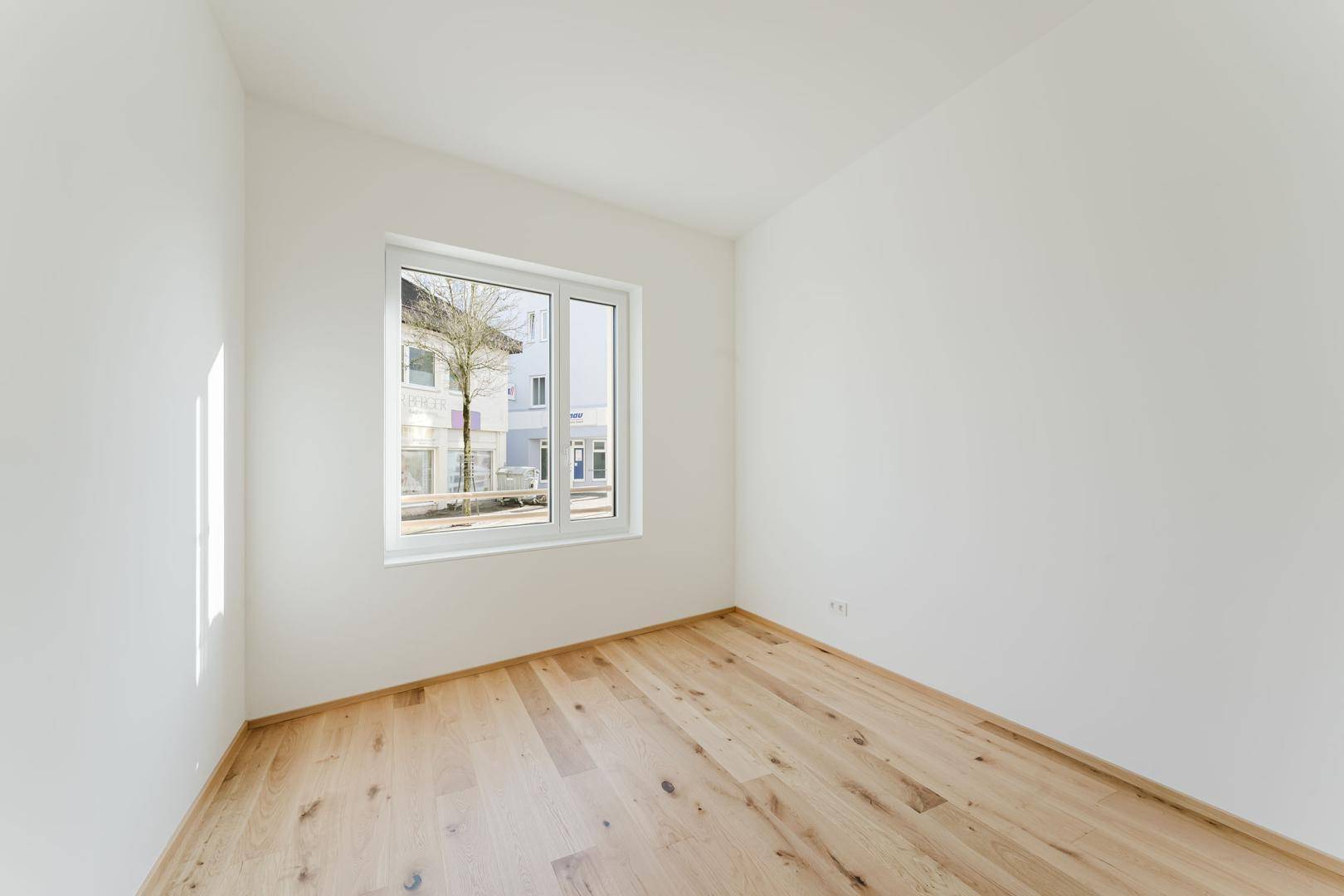 Lichtdurchflutetes, unmöbliertes Zimmer mit Holzboden und Blick nach draußen.