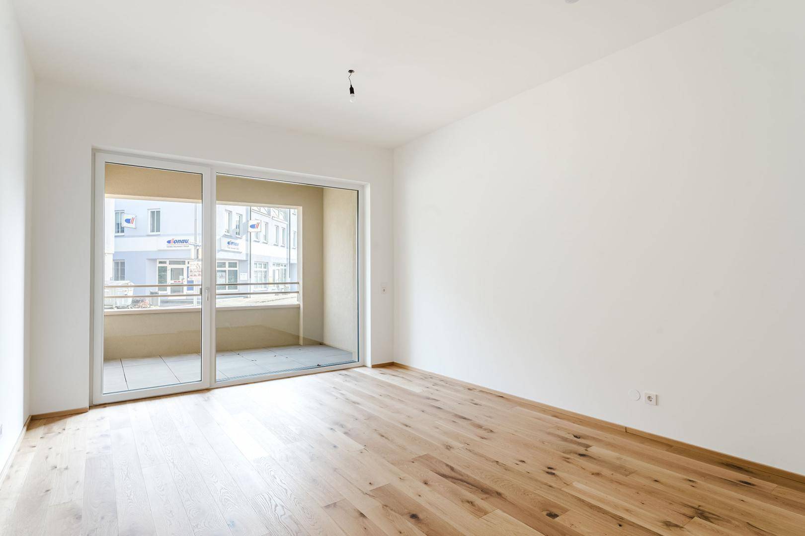 Geräumiges, helles Wohnzimmer mit Holzboden und direktem Zugang zum Balkon.
