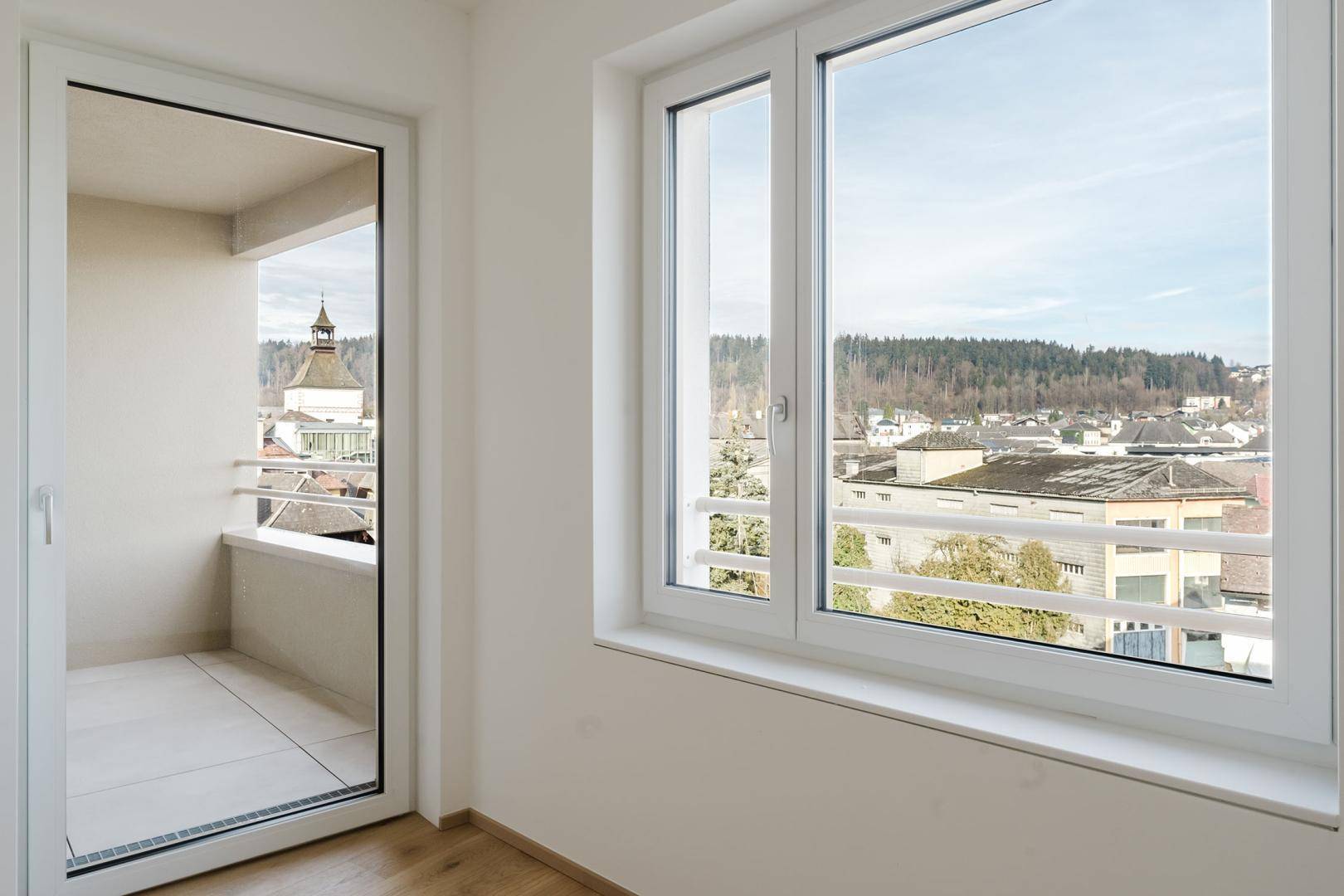 Fenster und Balkontür bieten einen Ausblick auf die Stadt und die umliegende Landschaft.