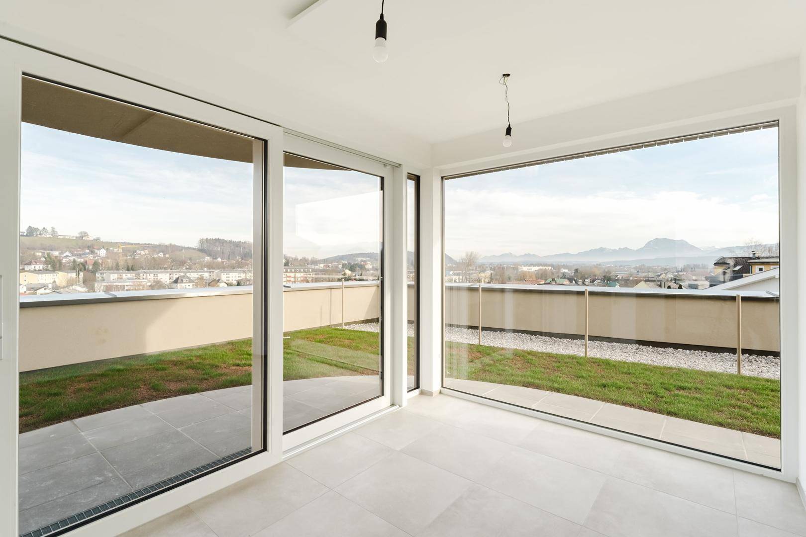 Heller Raum mit großen Fenstern, die einen weiten Blick auf die Berge und Grünflächen bieten.