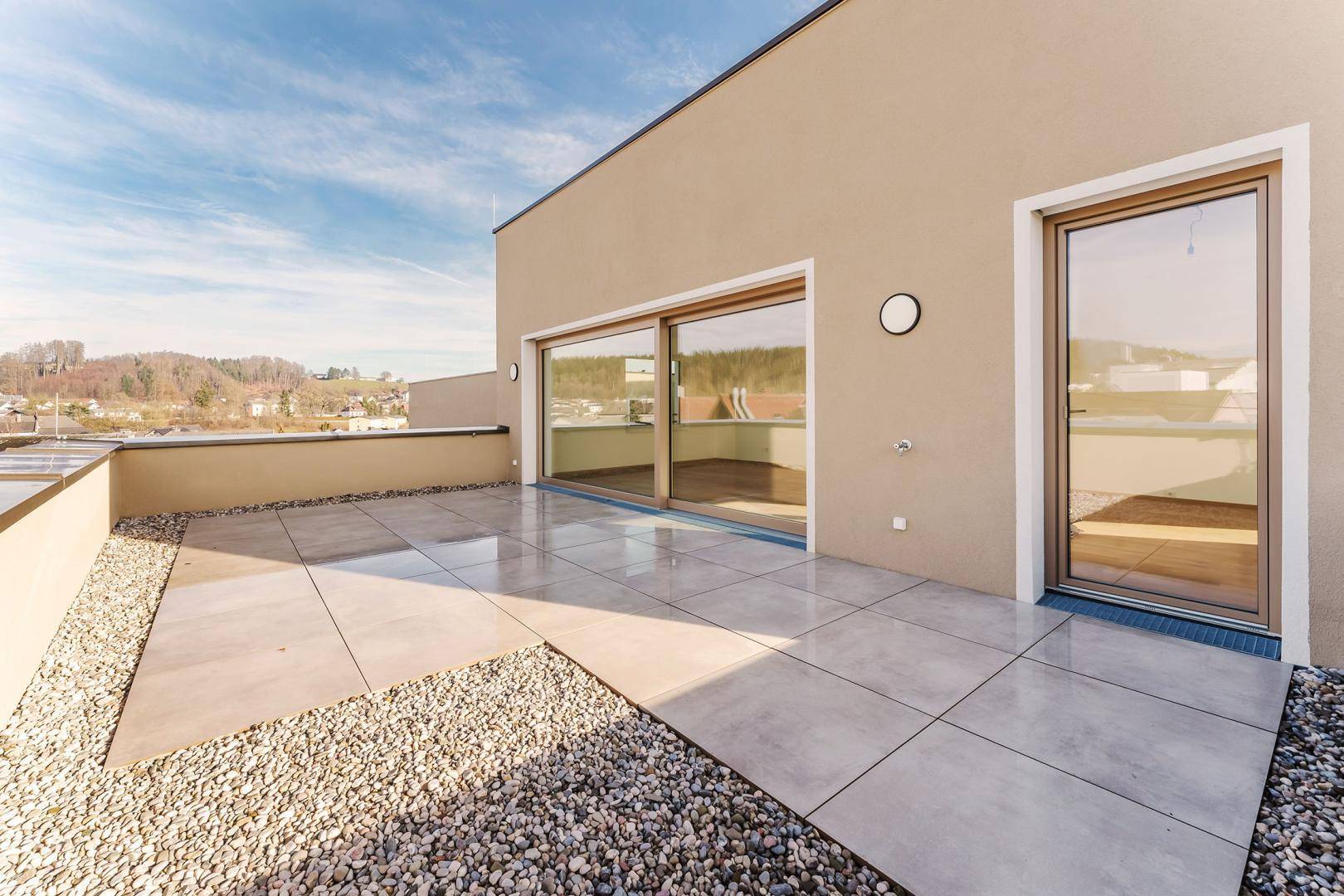 Große, geflieste Terrasse mit Kiesflächen und Zugang zu den Innenräumen des Gebäudes.