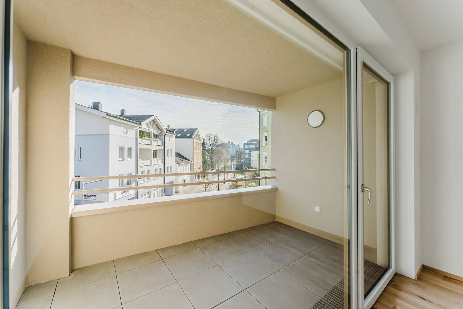Geräumiger, leerer Balkon mit Fliesenboden und Blick auf die städtische Umgebung.