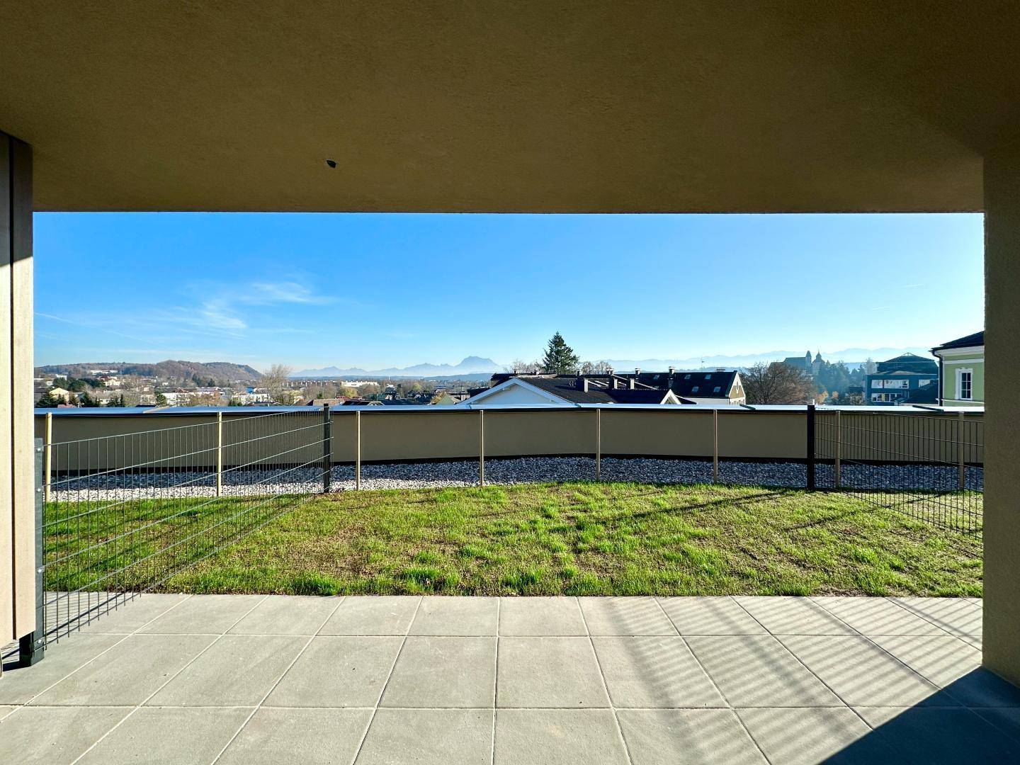 Große, unmöblierte Terrasse mit direktem Zugang zur Rasenfläche und weitem Bergblick an einem sonnigen Tag.