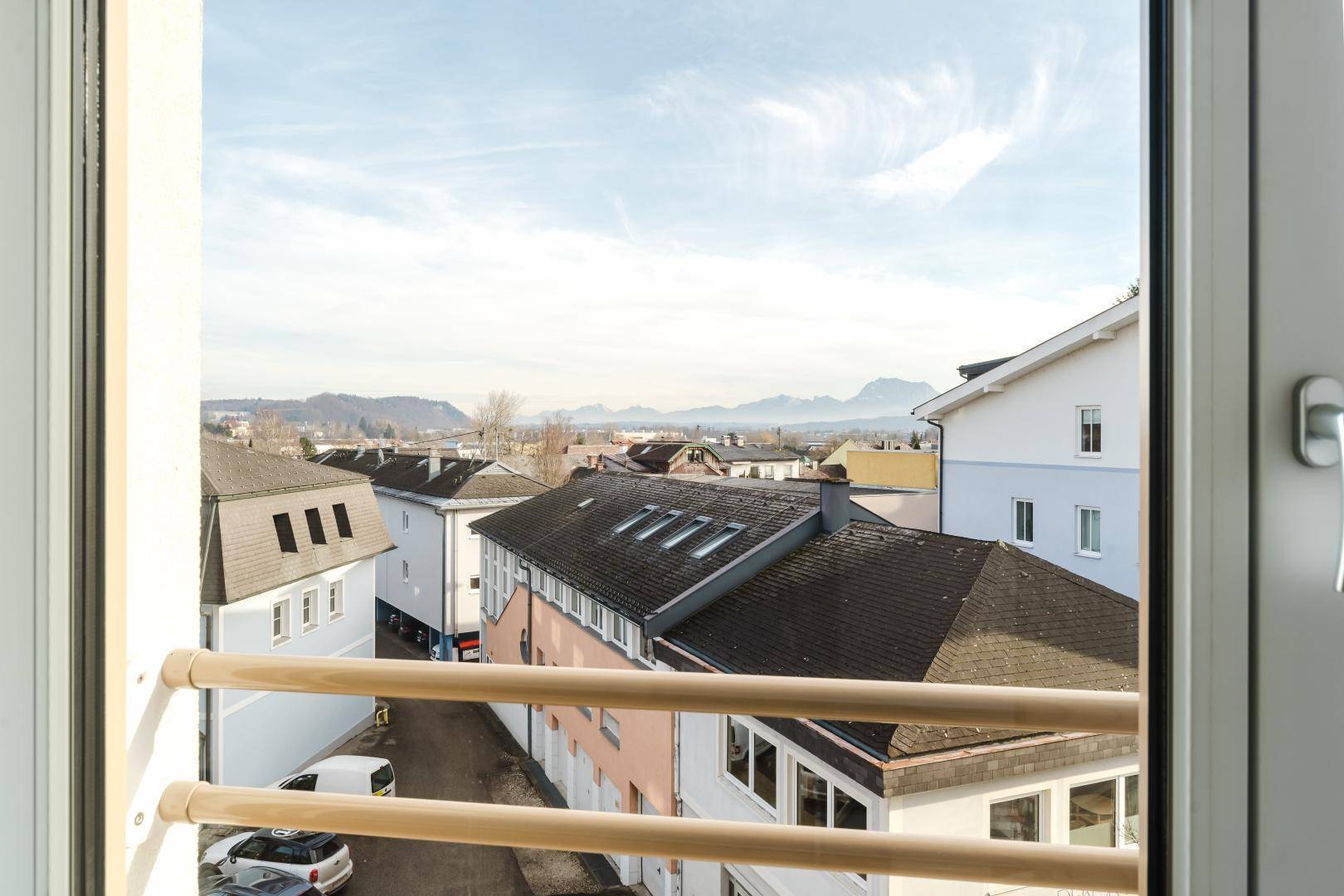 Ausblick aus dem Fenster auf die Dächer der Stadt, eine Straße und die malerische Bergkulisse in der Ferne.