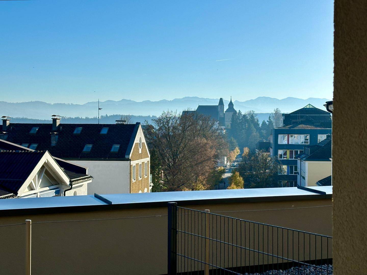 Panoramablick von einem Balkon auf die Stadt, eine Kirche und die beeindruckende Bergkette am Horizont.