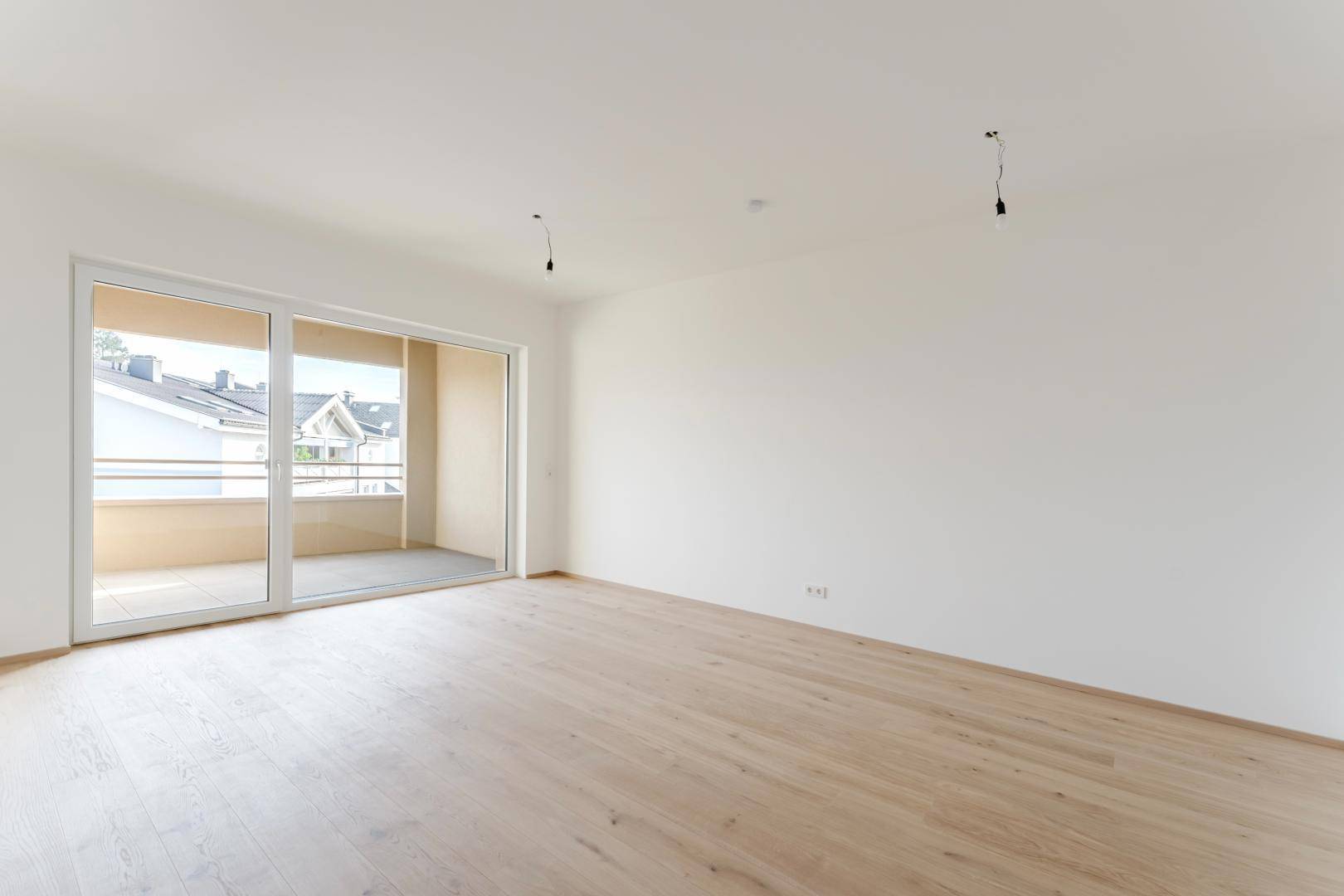 Geräumiges, unmöbliertes Wohnzimmer mit Parkettboden und viel Tageslicht durch die große Fensterfront.