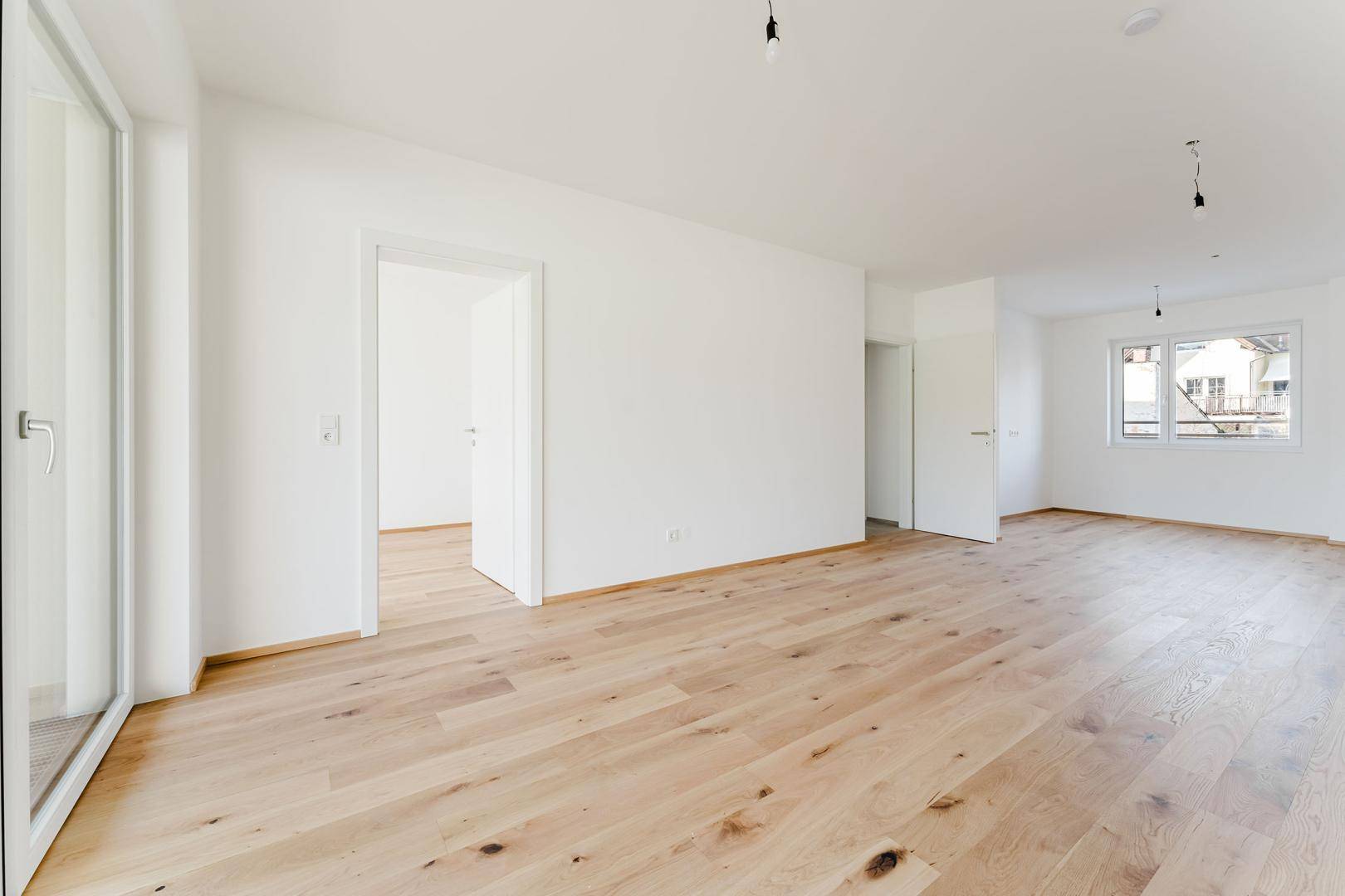 Geräumiges, helles Zimmer mit Holzboden und mehreren Türen, bereit für die Einrichtung.