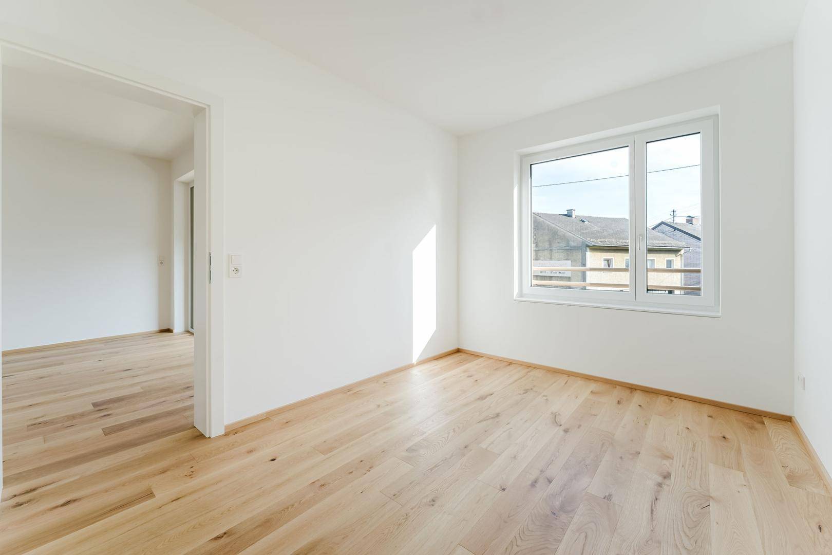 Sonniger Raum mit Holzboden und weiß gestrichenen Wänden, ideal als Schlaf- oder Arbeitszimmer.