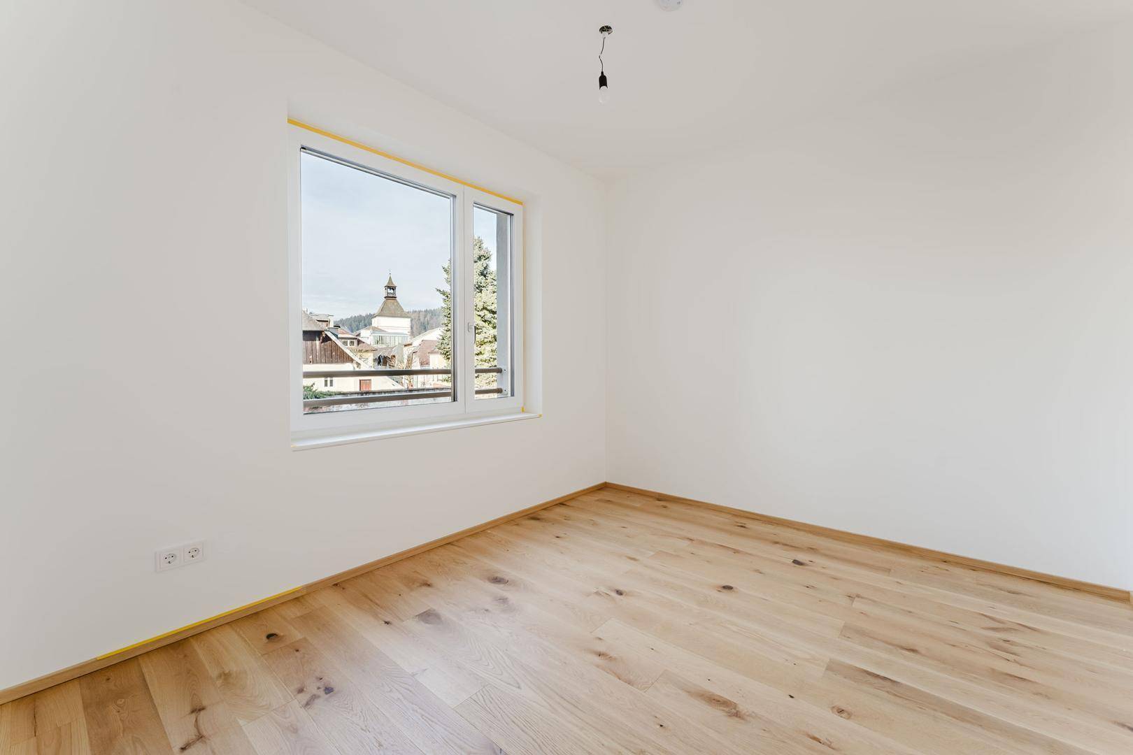 Helles Schlafzimmer mit Holzboden und Fensterblick auf die umliegende Bebauung und Natur.