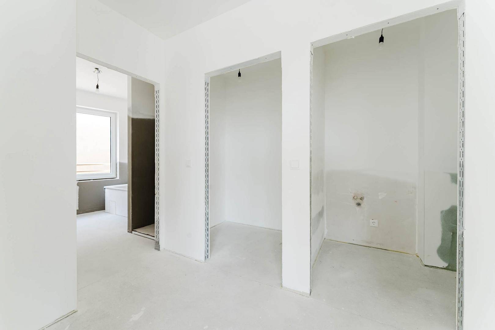Unfertiger Innenraum mit Rohbauwänden und Blick in ein Badezimmer mit Fenster.