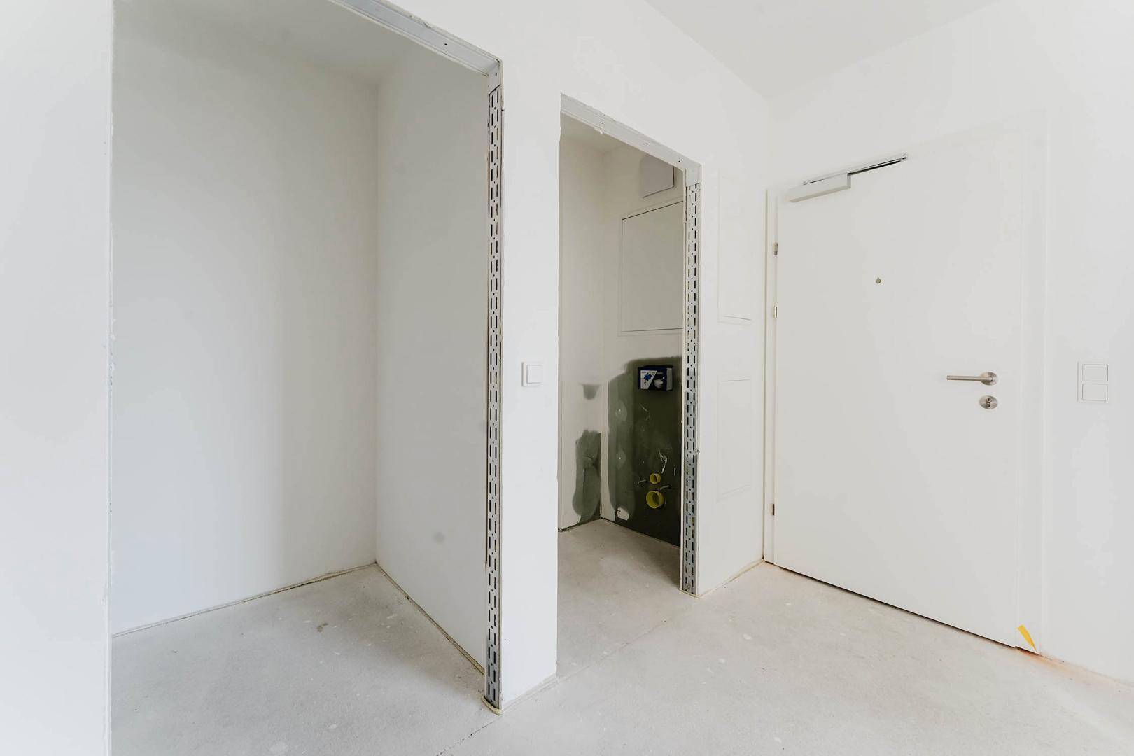 Unfertiger Eingangsbereich mit weißer Tür und Rohbauwänden, bereit für den Ausbau.