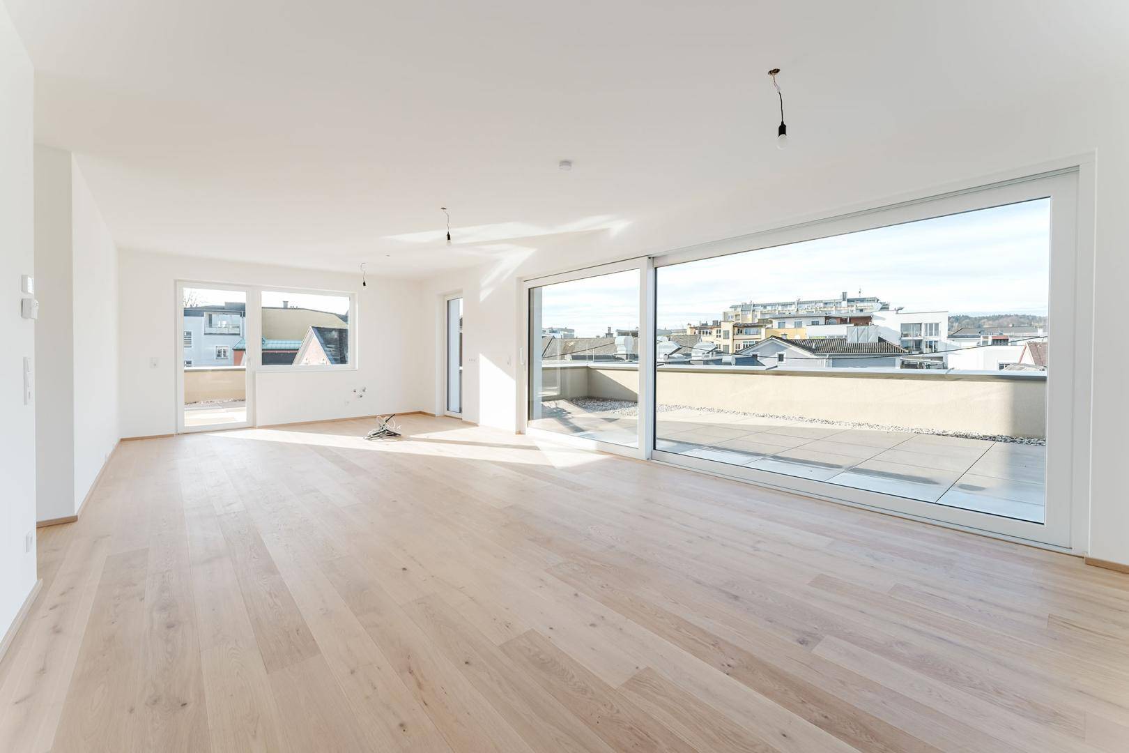Geräumiger, heller Wohnraum mit großen Fensterfronten und Zugang zu einer weitläufigen Terrasse.