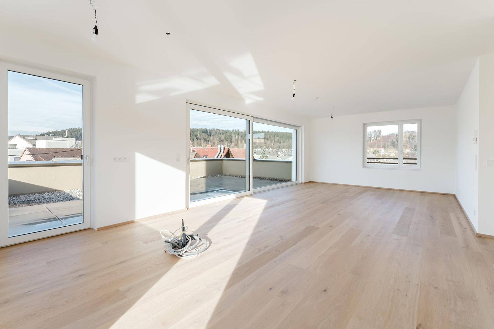Heller, leerer Wohnraum mit großen Schiebetüren zur Terrasse und hellem Parkettboden.