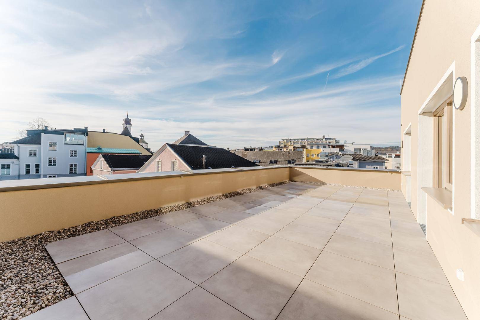 Große Dachterrasse mit hellen Fliesen und Kies, bietet einen weiten Blick über die Stadt.