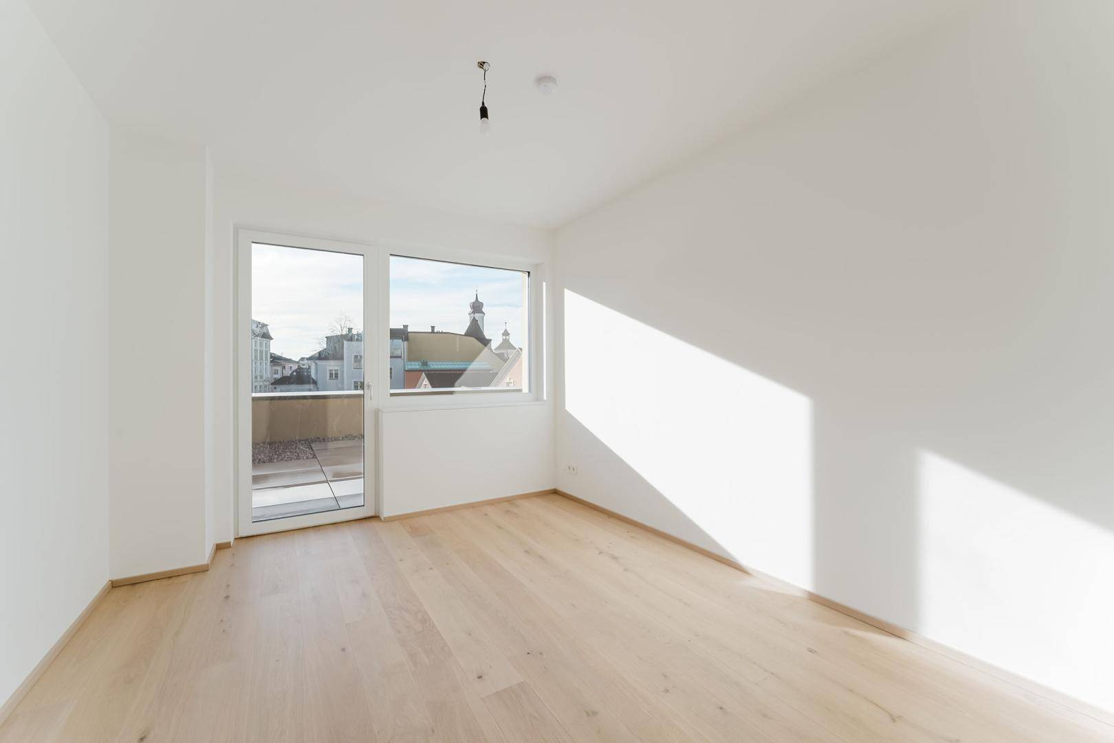 Helles Schlafzimmer mit Holzboden und Zugang zu einem Außenbereich, sonnendurchflutet.