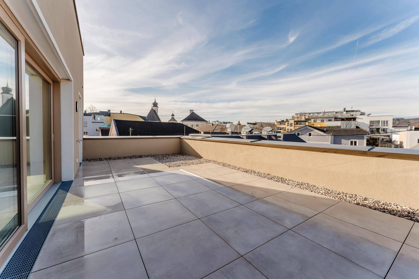 Geräumige, geflieste Terrasse mit Kiesstreifen und Blick auf die Dächer der Stadt.