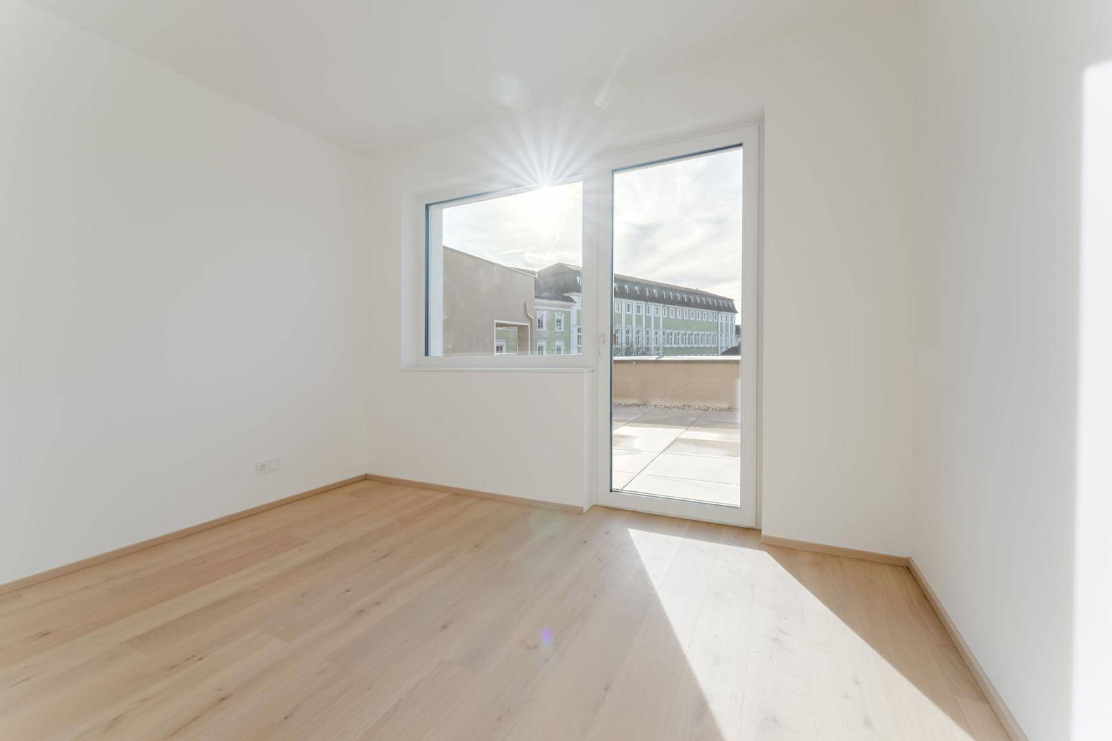 Lichtdurchflutetes Zimmer mit hellem Holzboden und großem Fenster, das viel Sonnenlicht hereinlässt.