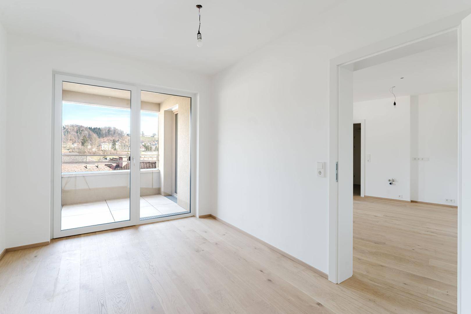 Heller Raum mit Parkettboden und Schiebetür zum Balkon, bietet Weitblick.