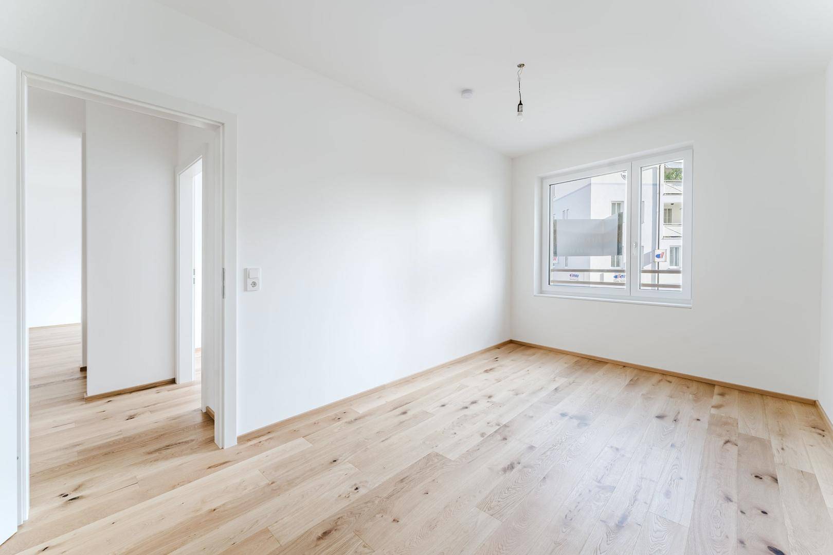 Leeres Zimmer mit hellem Holzboden und Fenster, bereit zur individuellen Gestaltung.