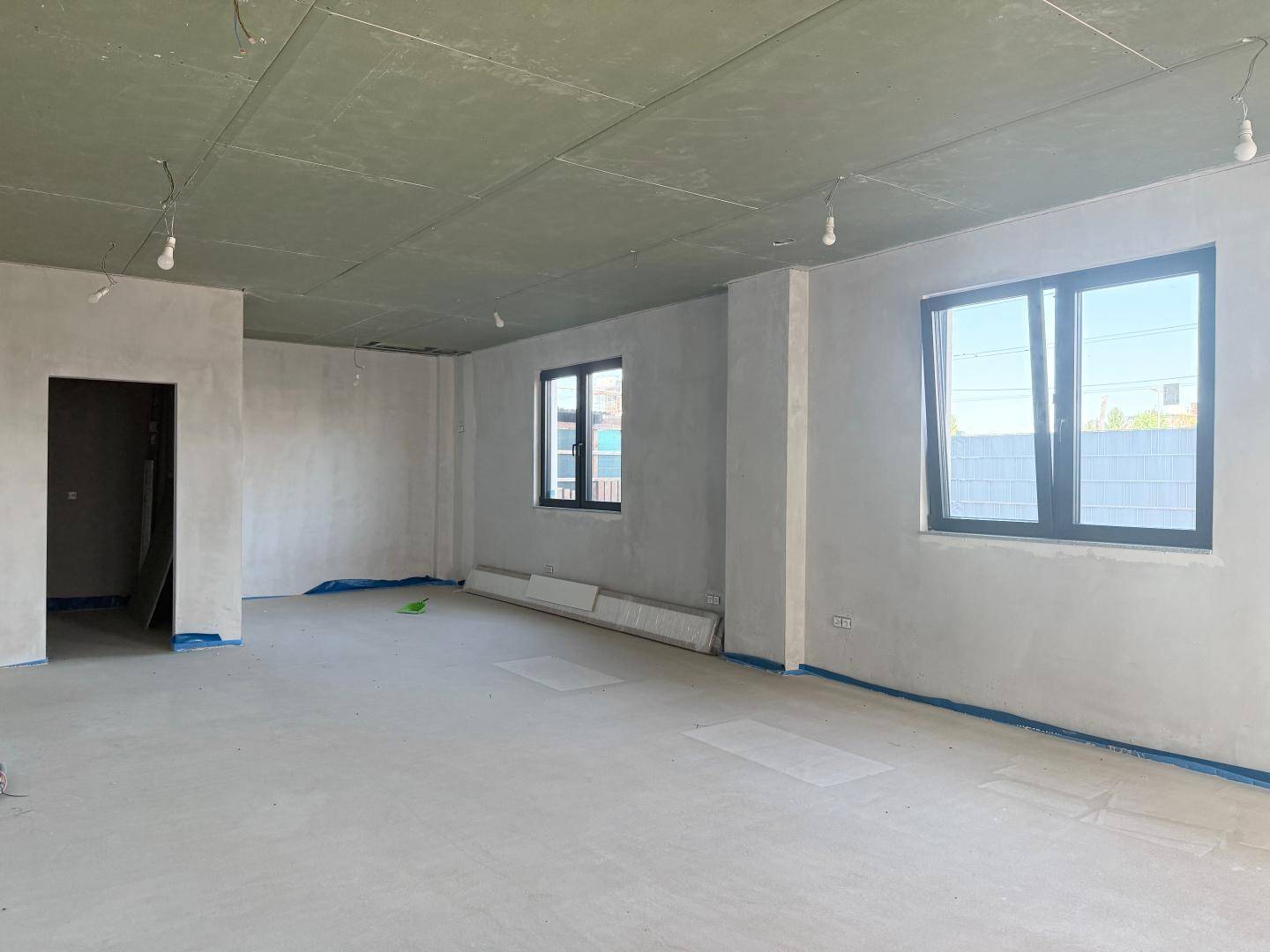 Unfertiger Gewerberaum mit Rohbauwänden, Betonboden und großen Fenstern, bereit für den Ausbau.