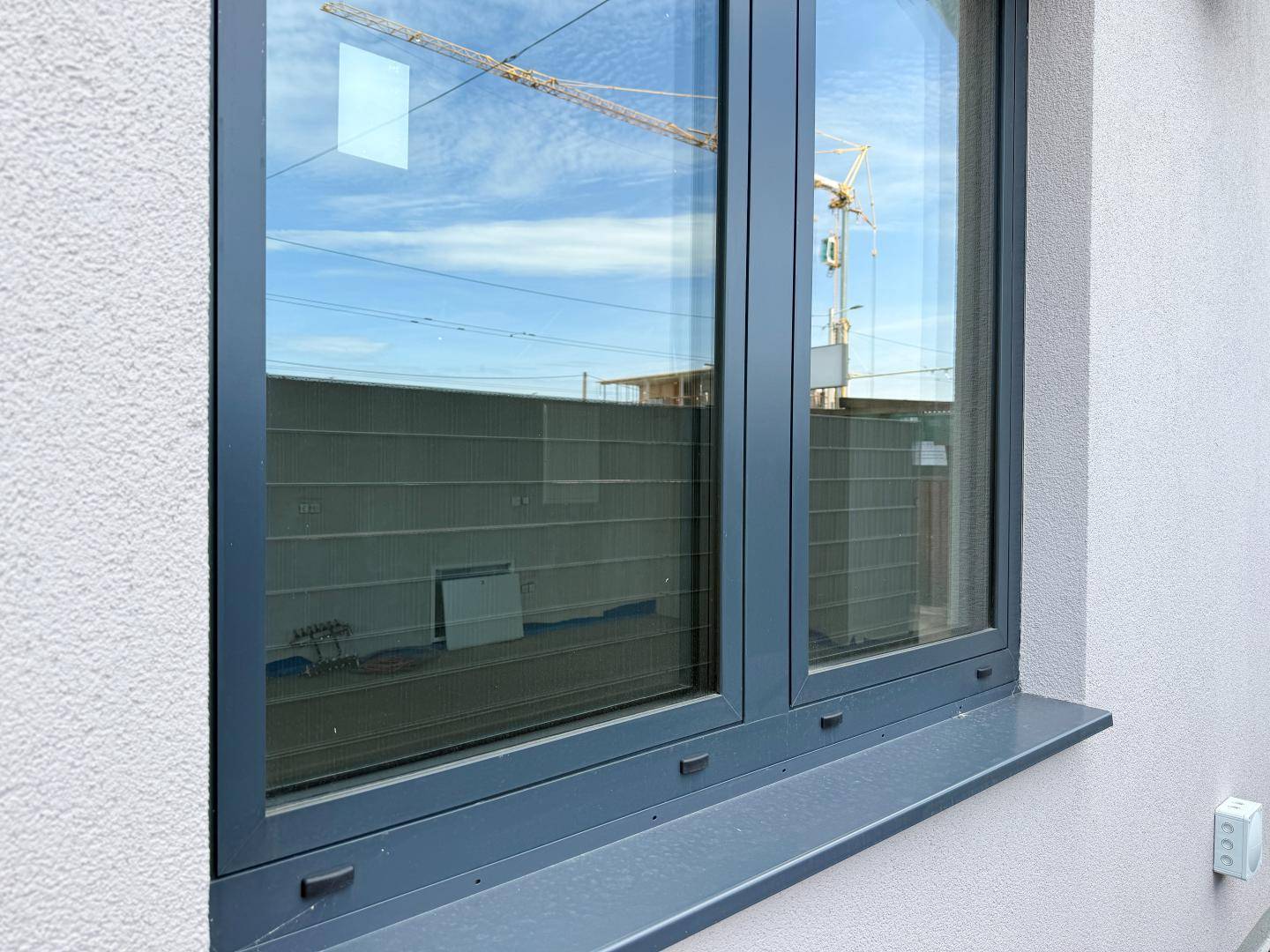 Außenansicht eines Fensters mit Blick auf eine Baustelle und einen Kran im Hintergrund.