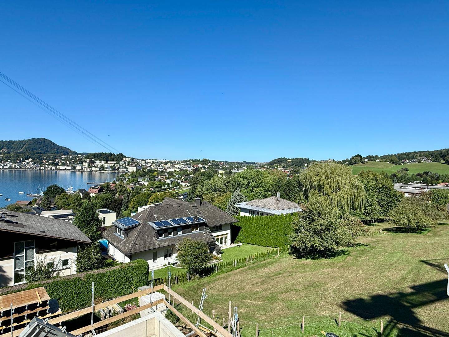 Weitläufiger Blick über die Nachbarschaft mit See im Hintergrund und grünen Hügeln unter blauem Himmel.