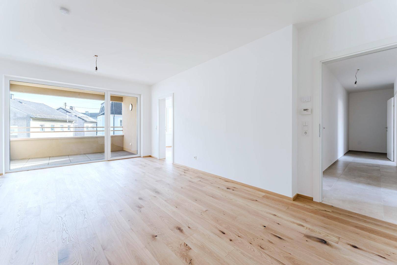 Geräumiges Zimmer mit Holzparkett, weiß gestrichenen Wänden und Balkonzugang.