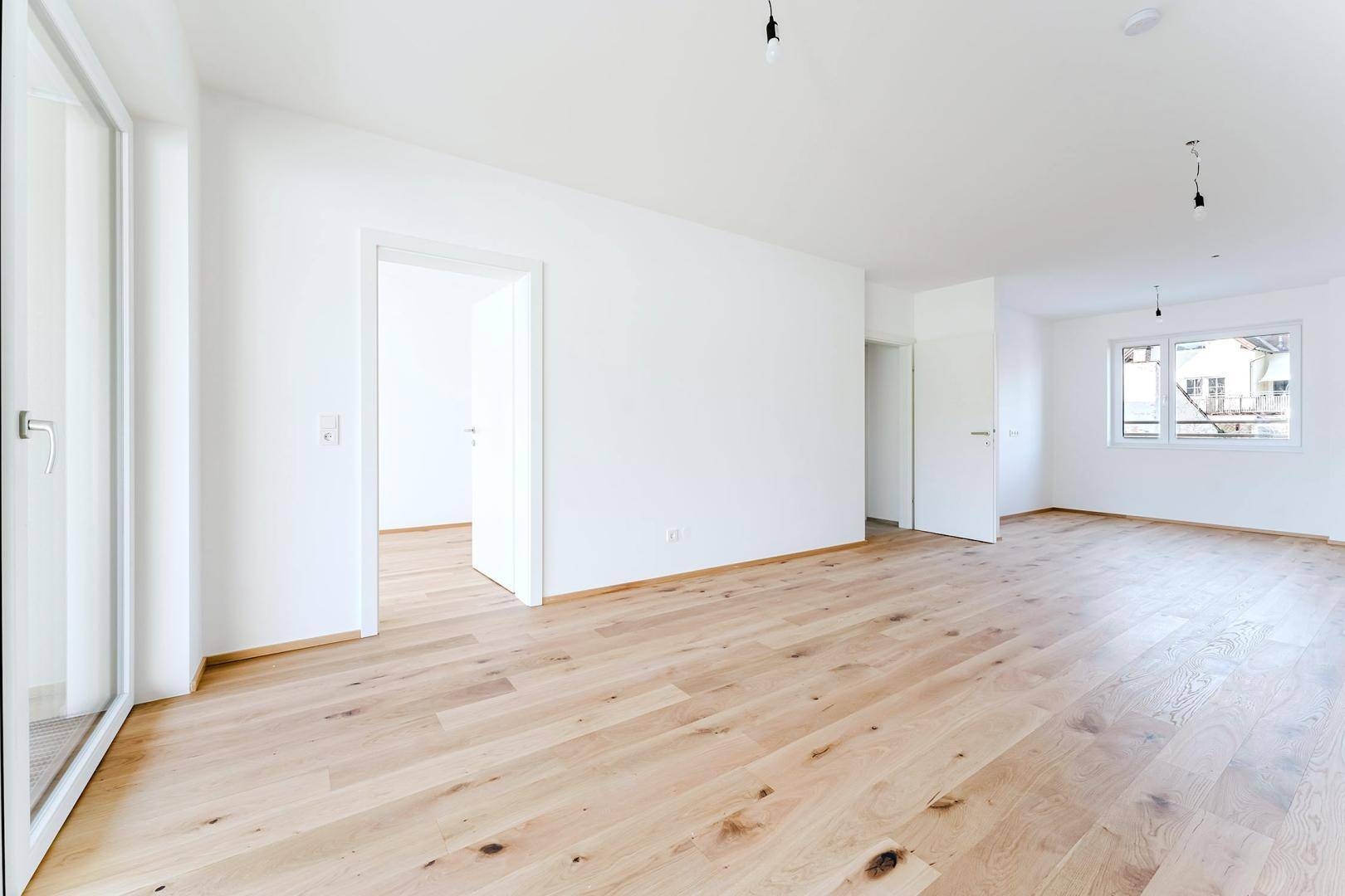 Helles, unmöbliertes Zimmer mit Holzfußboden und großzügigem Zugang zum Balkon.