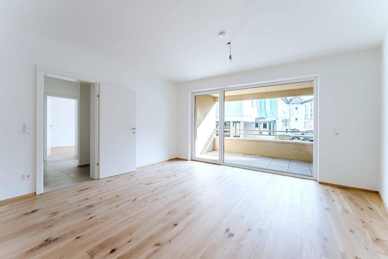 Geräumiges, unmöbliertes Zimmer mit Holzparkett und großem Schiebetürzugang zum Balkon.